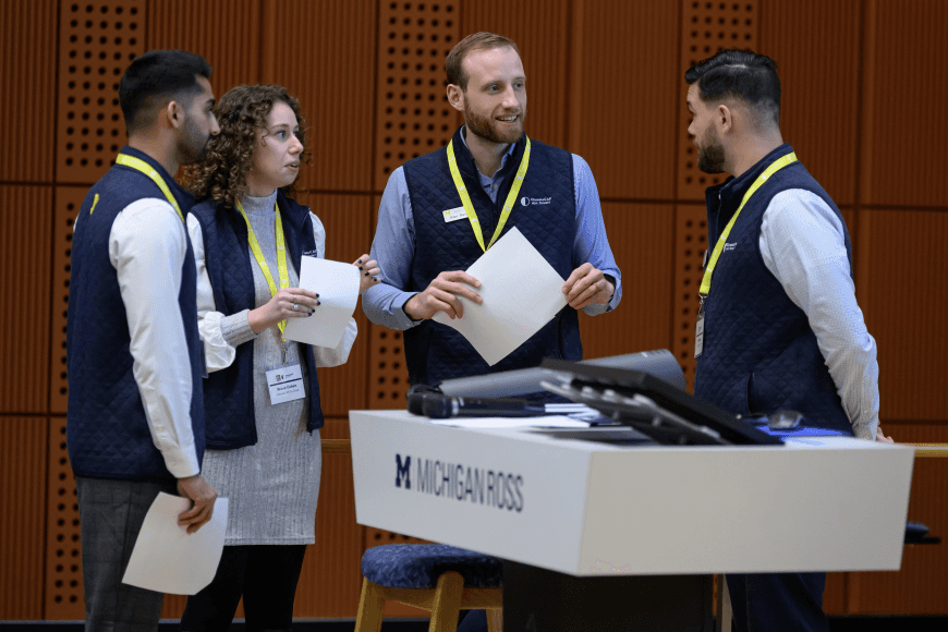 Four people in matching outfits gather around a table, discussing documents in a meeting setting.