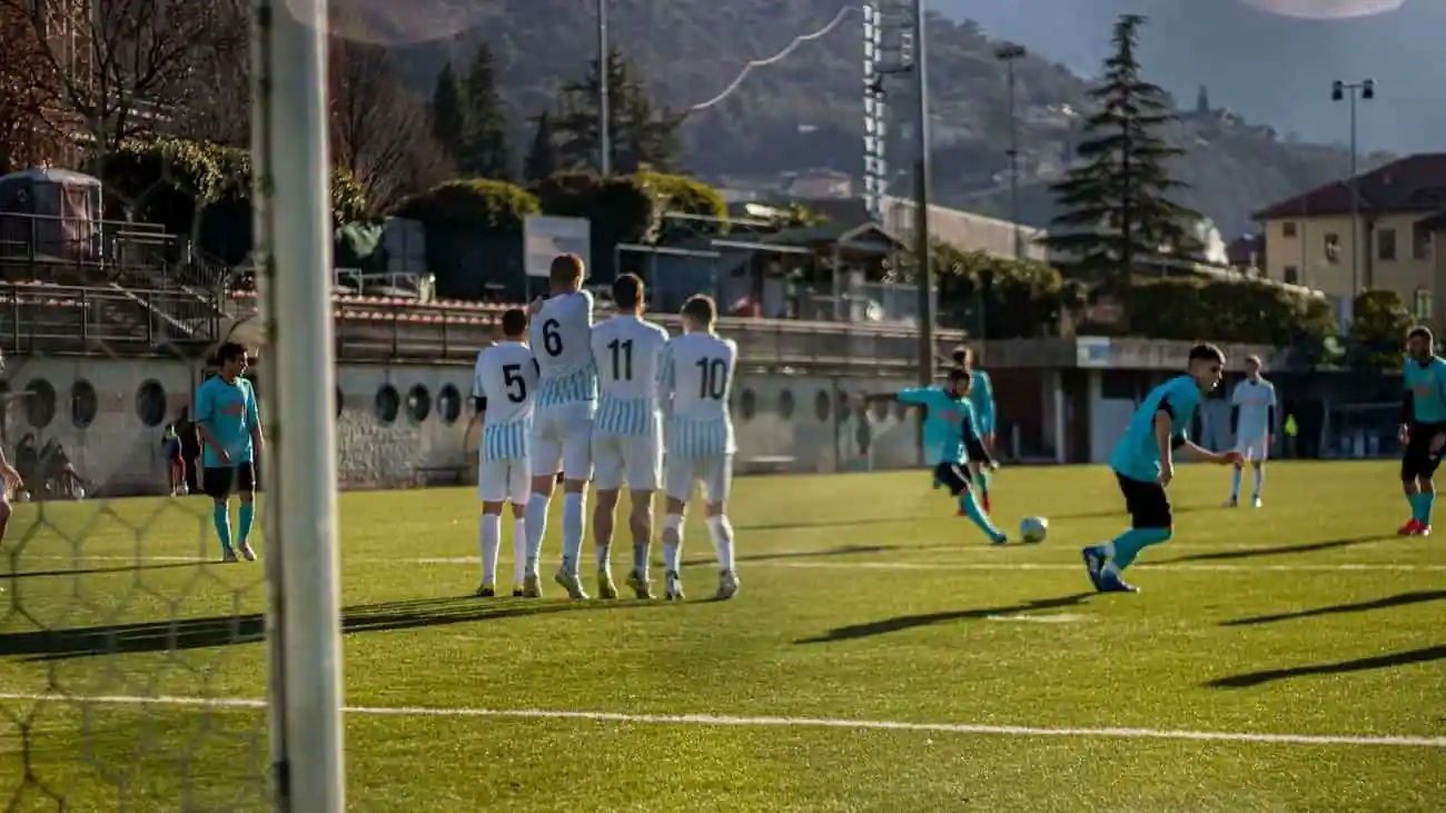 Spieler in gestreiften Trikots stehen in Reihen auf einem sonnigen Platz während eines alternativen Liga-Fußballspiels und symbolisieren den Geist des Wettbewerbs und der Gemeinschaft abseits des kommerziellen Profifußballs.