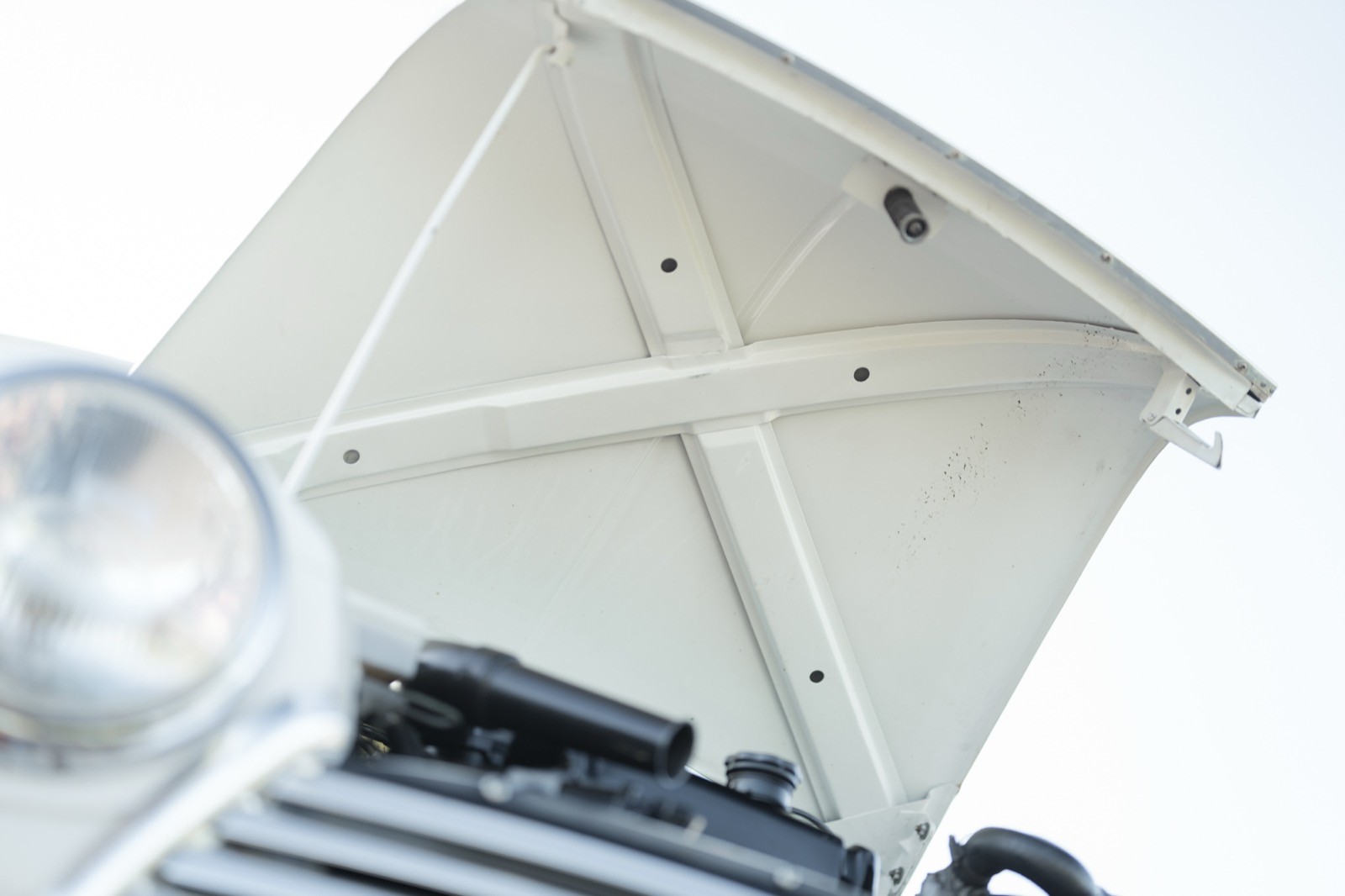 Close-up of a car hood lifted, revealing the engine compartment beneath, against a bright background.