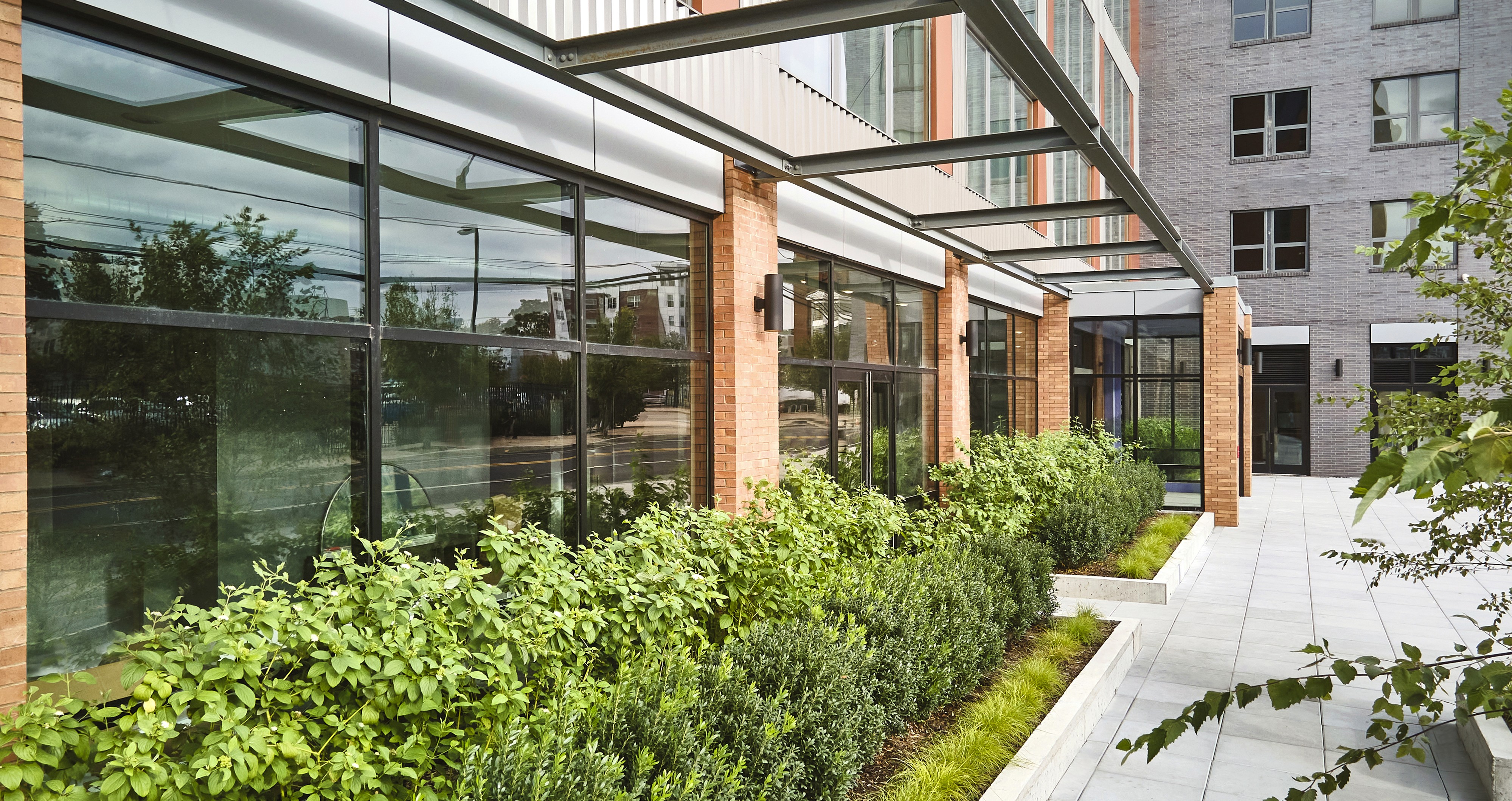 A modern building with large windows overlooking a landscaped area featuring greenery and a pathway.