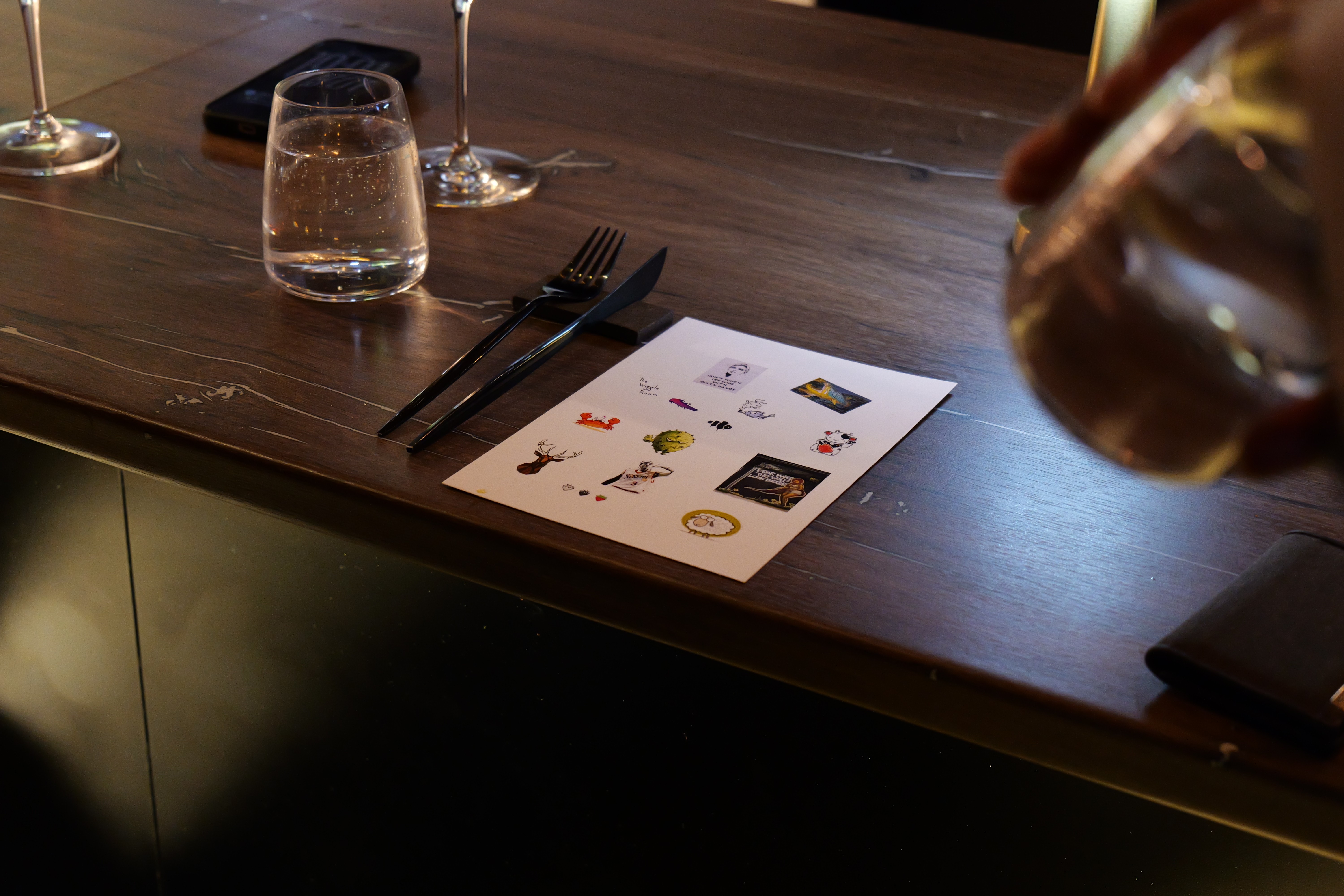 Wooden outdoor table set with multiple plates of food, including dips, salads, potatoes with cheese, and glasses of water, with hands reaching in to eat.