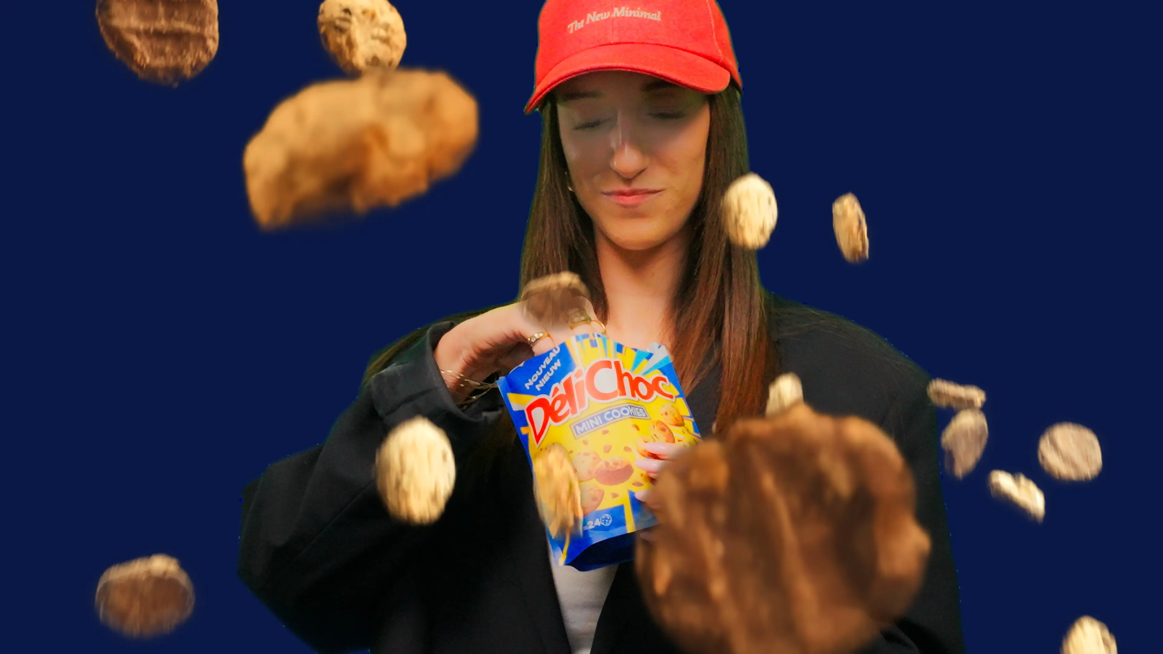 A person in a red cap holds a cookie while food items are floating around them against a blue background.