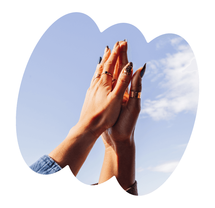 Two hands with rings and painted nails pressed together in a high-five gesture against a blue sky background.