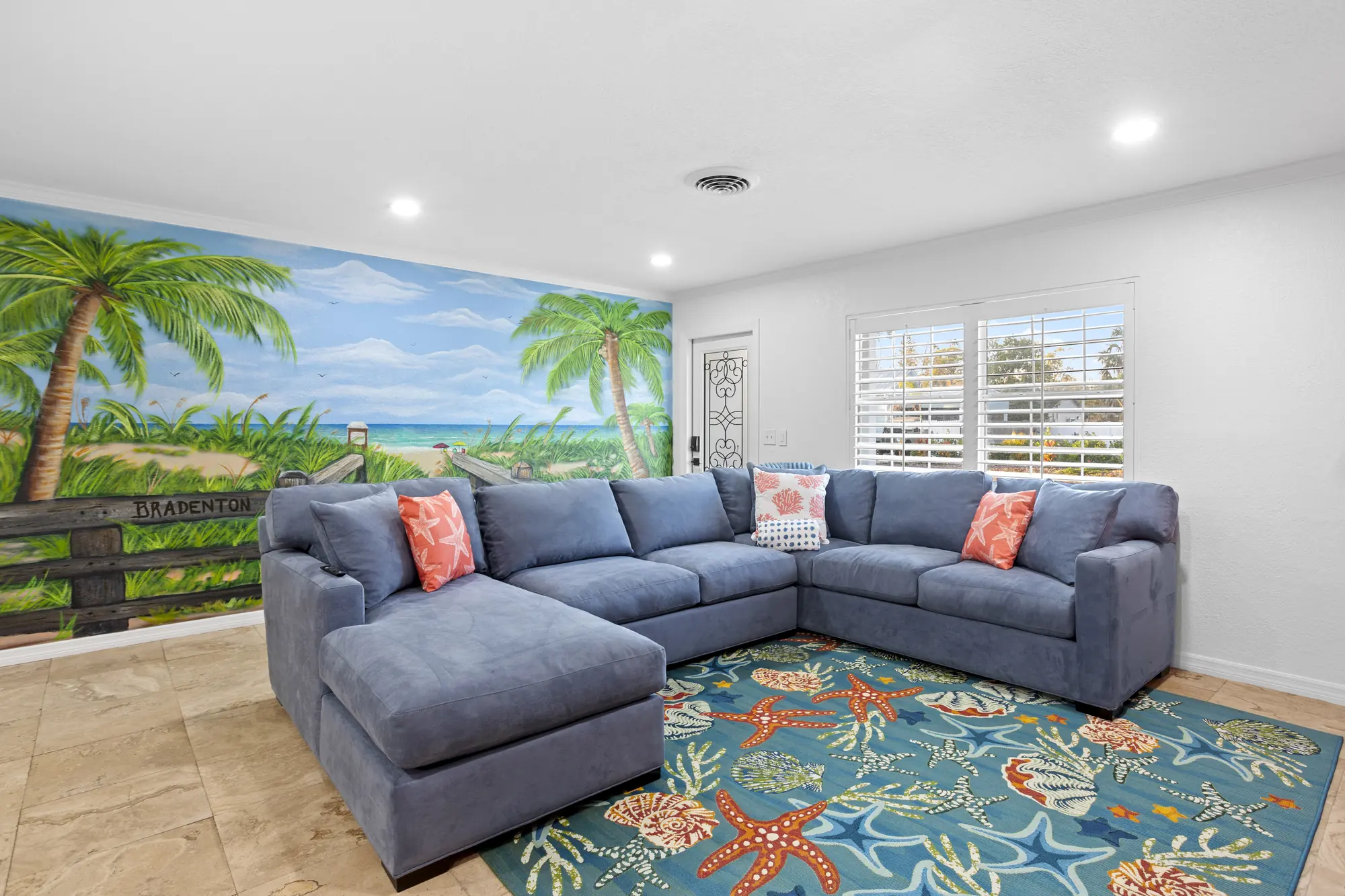 Living room with a blue sectional and a palm beach mural at Pickleball Resort, Bradenton, Florida