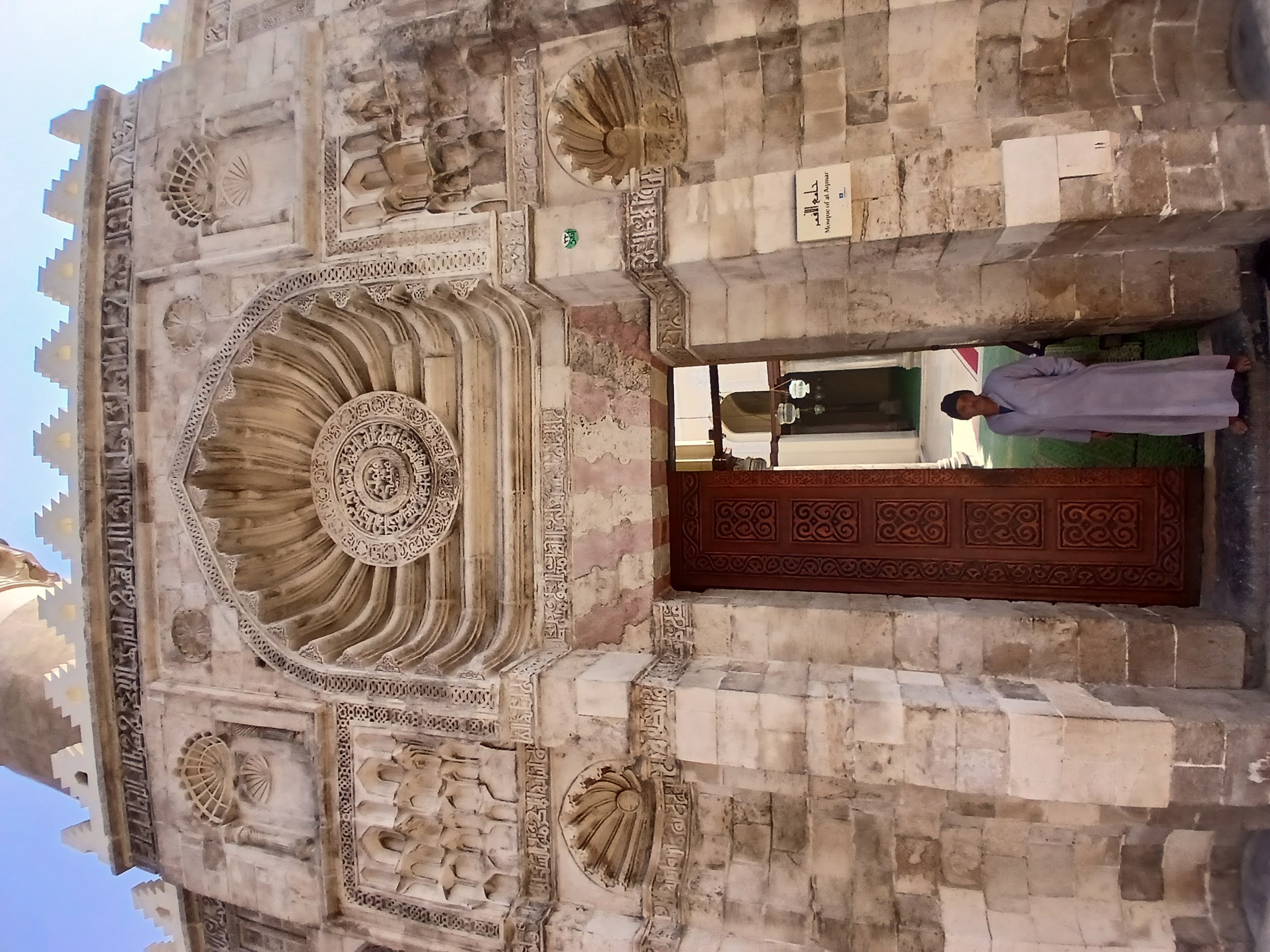 The front facade of Jame al Aqmar masjid in Cairo. the facade is decorated with intricate carvings of gemotric patterns and kufic arabic script