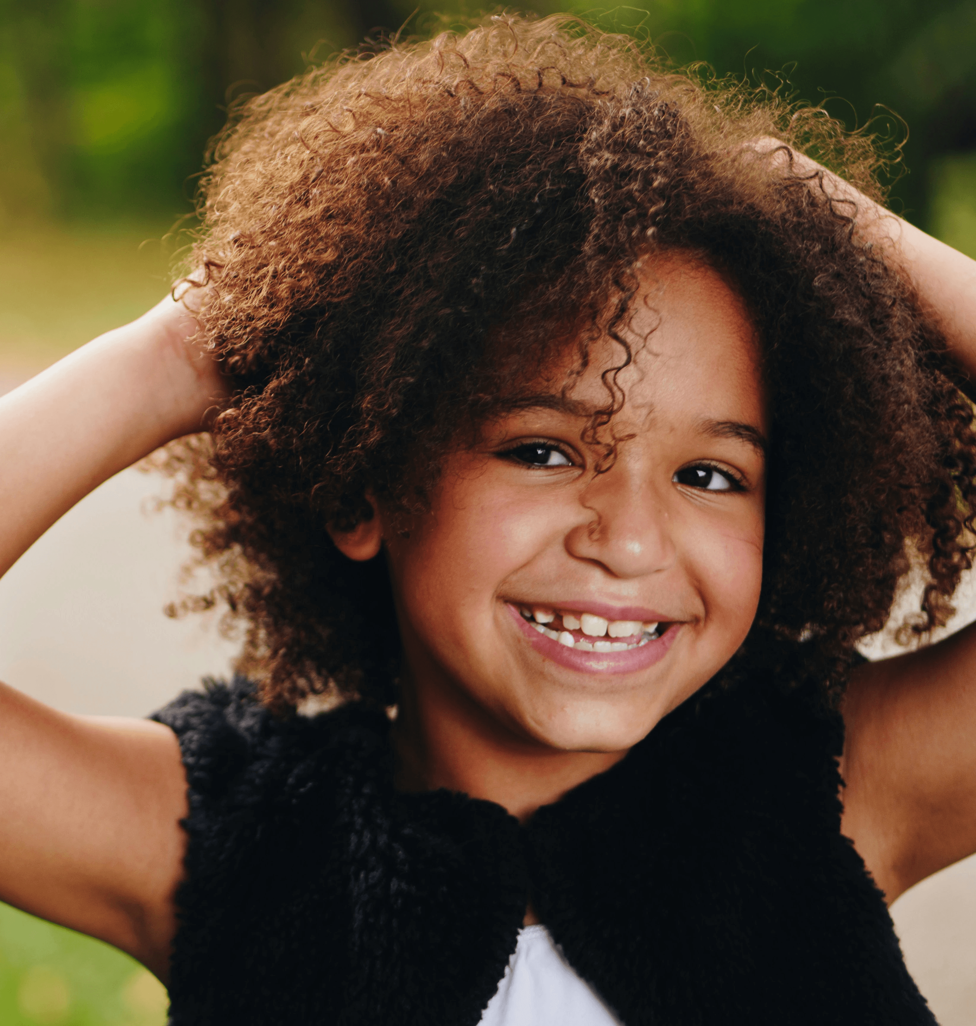 girl wearing black vest raising two hands near green grass field during daytime