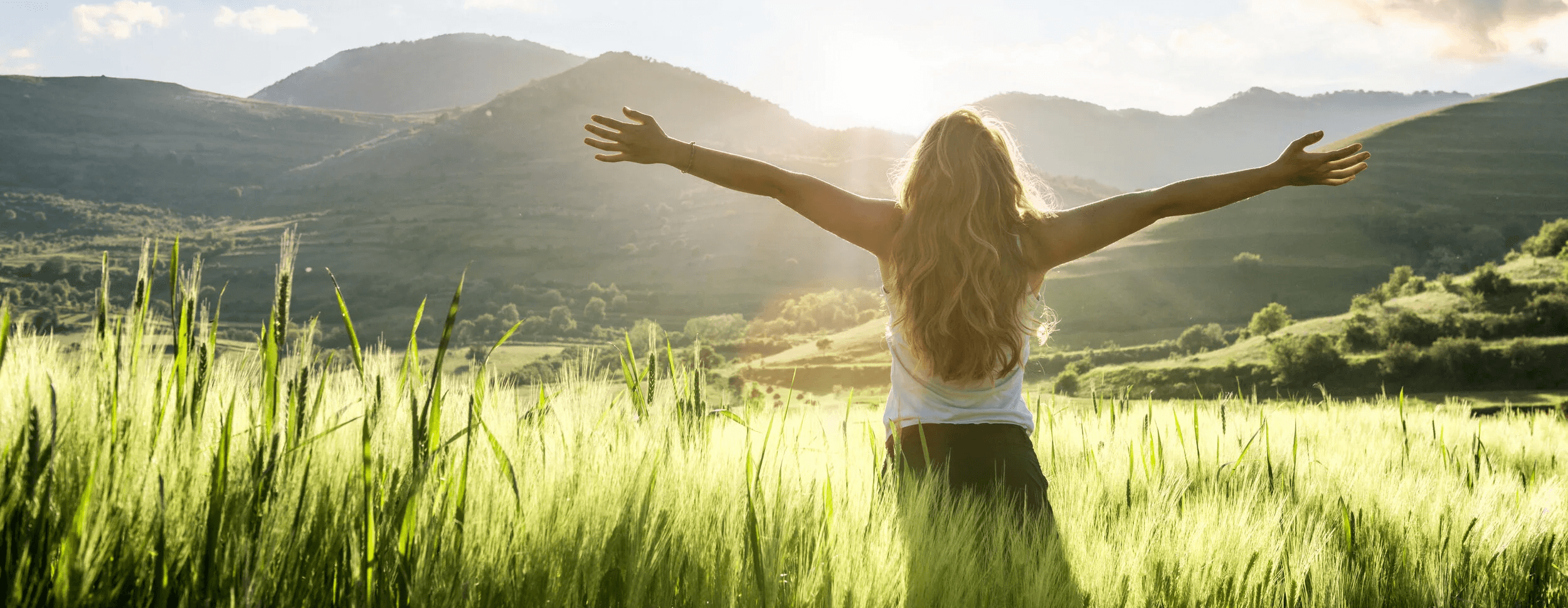 Eine blonde Frau, die Ihre Arme entgegen der Sonne ausbreitet.