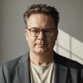 A smiling man in a suit and glasses, exuding confidence and professionalism.