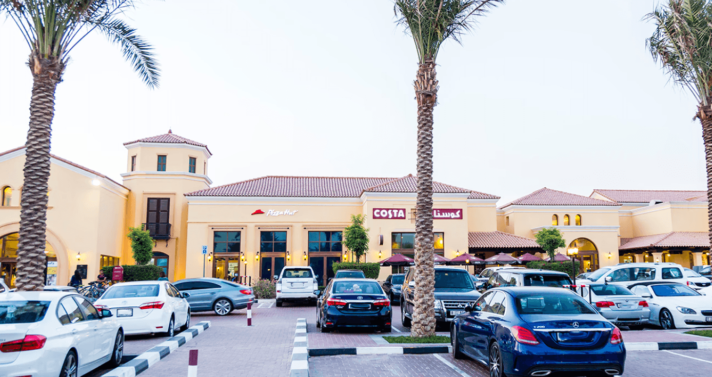 A parking lot filled with cars in front of the Arabian Ranches shopping center.