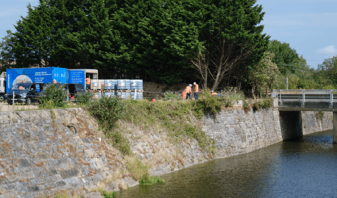 Engineers in orange PPE work beside a riverbank with Mainmark equipment, repairing and waterproofing substructure foundations