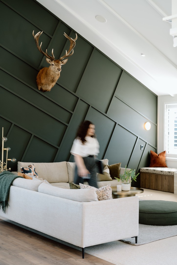 A green, white and gold minimalistic, architecturally designed kitchen with a women walking behind the kitchen bench, blurred