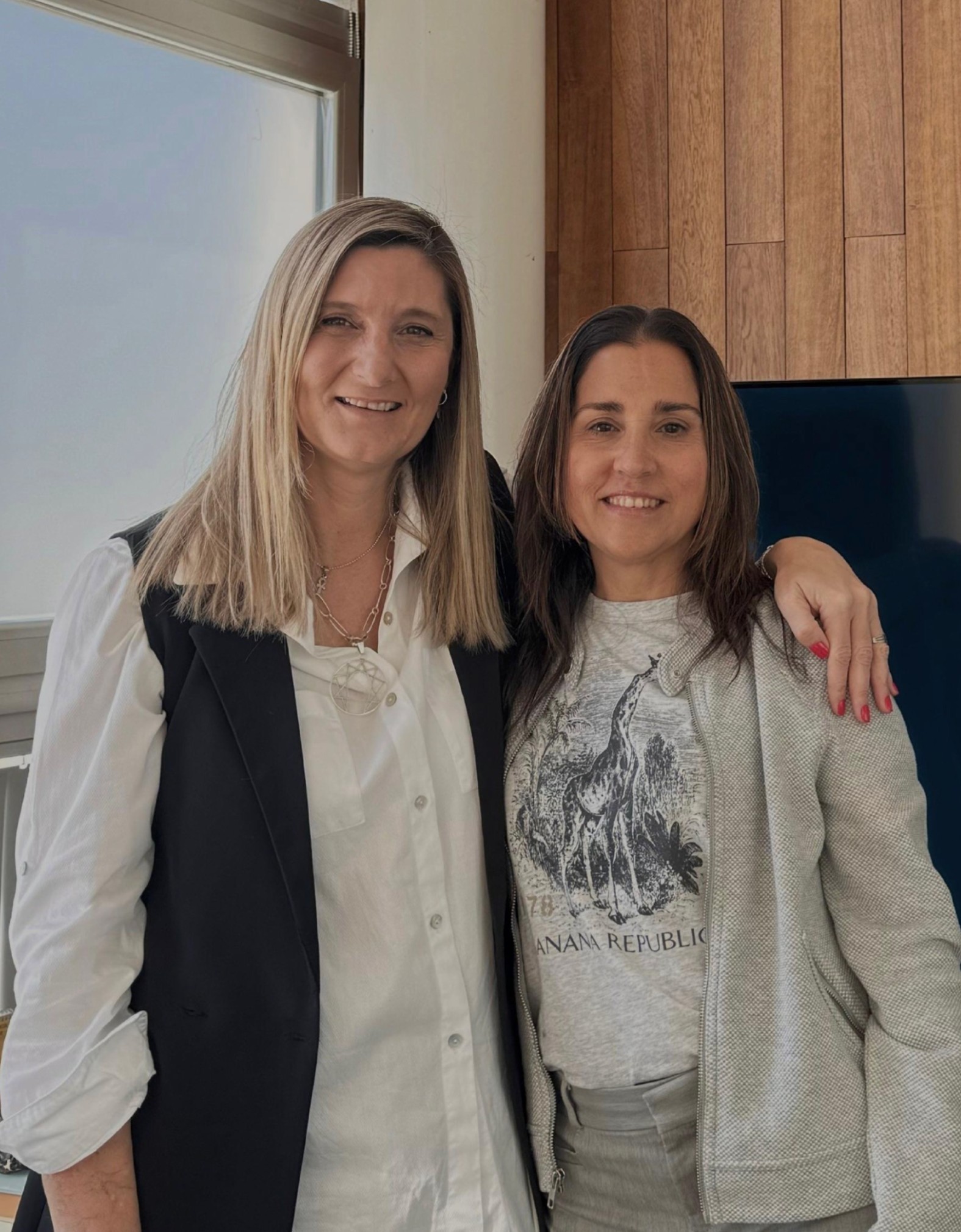 Smiling female therapist with short gray hair, wearing a brown top and a purple shawl, surrounded by a cozy background.