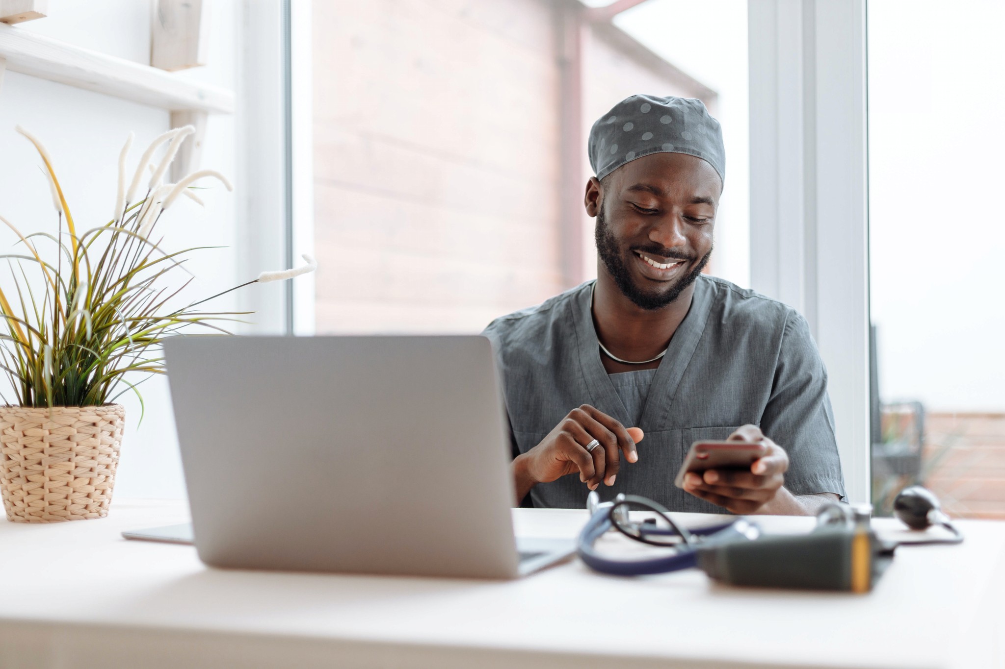 Male doctor smiling sitting at desk using phone