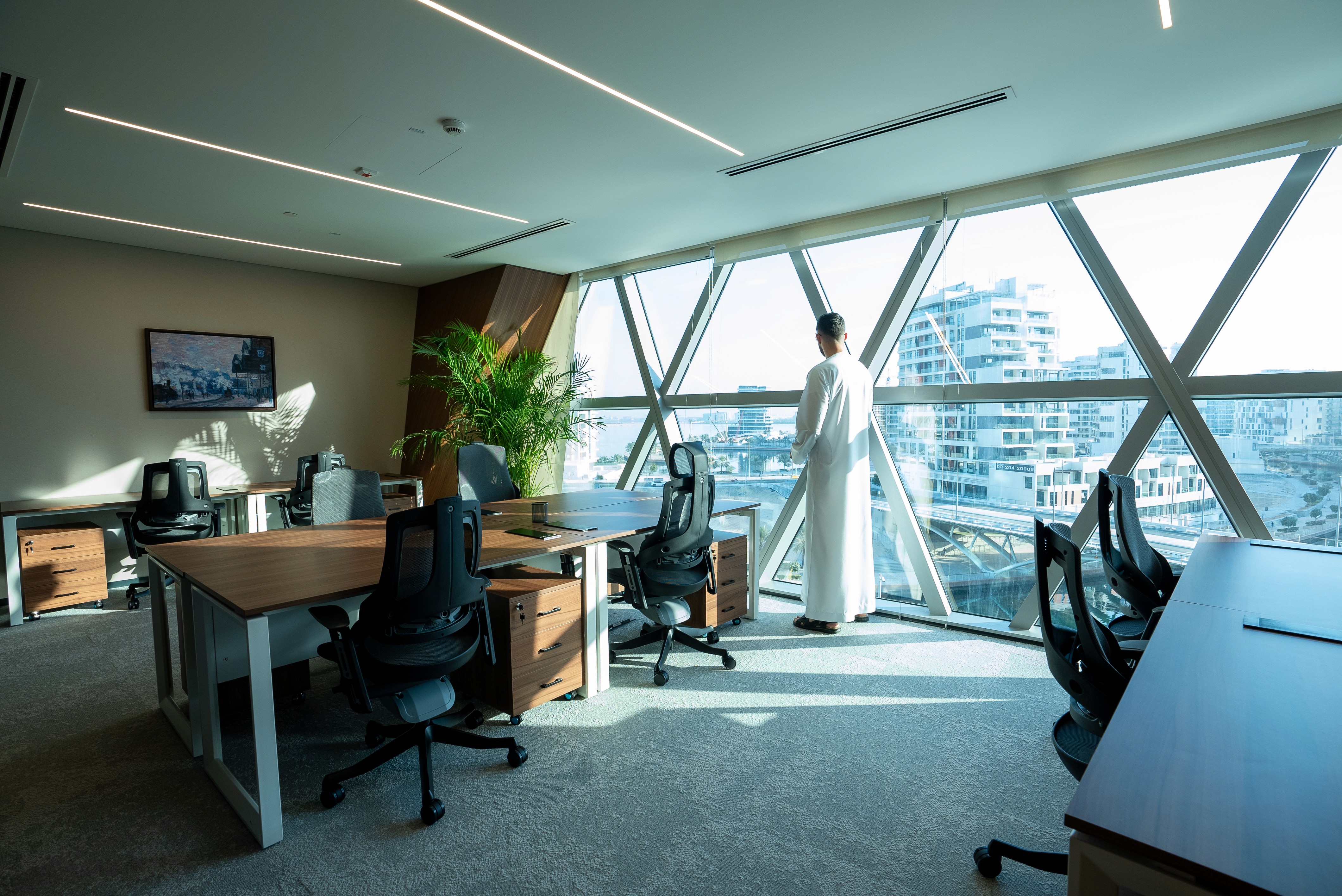 Open-plan coworking area in serviced office spaces in Dubai with stylish desks, ergonomic chairs, and natural greenery.