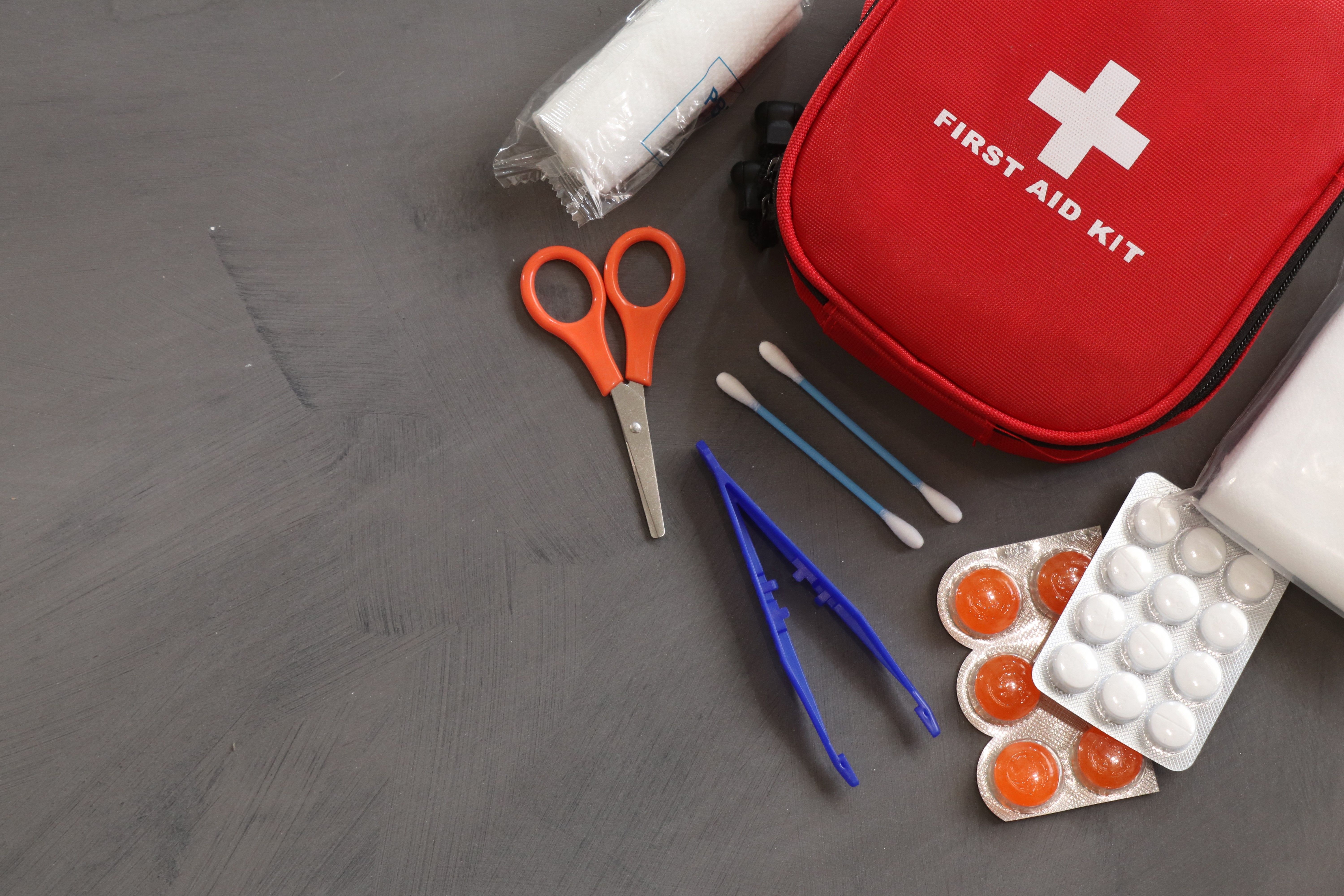 First Aid Kit on the floor with utensils and tools next to a red bag