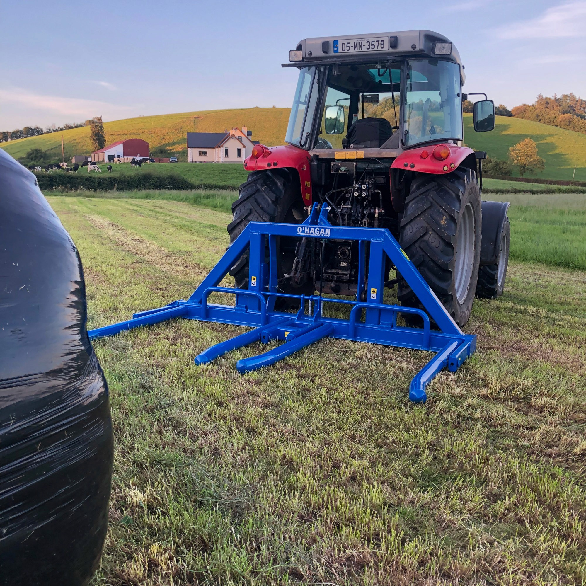 Massey Ferguson Red Tractor in a farm field with blue hydraulic folding bale handler attached ready to lift a black bale