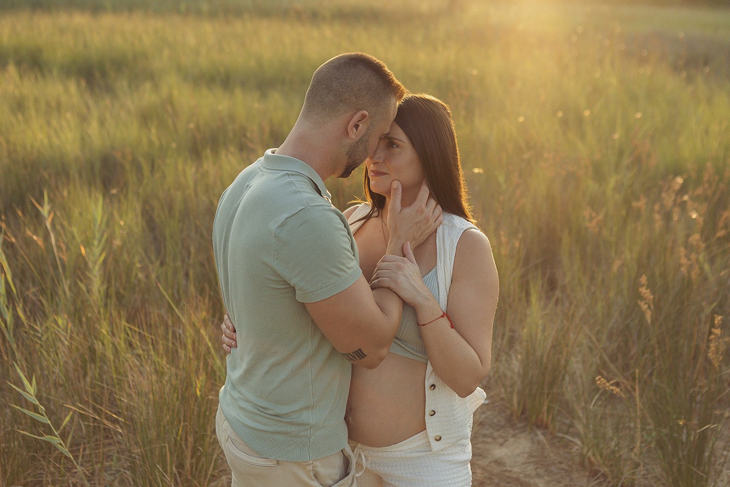 Pareja abrazándose durante una sesión de embarazo al aire libre con enfoque emocional y natural