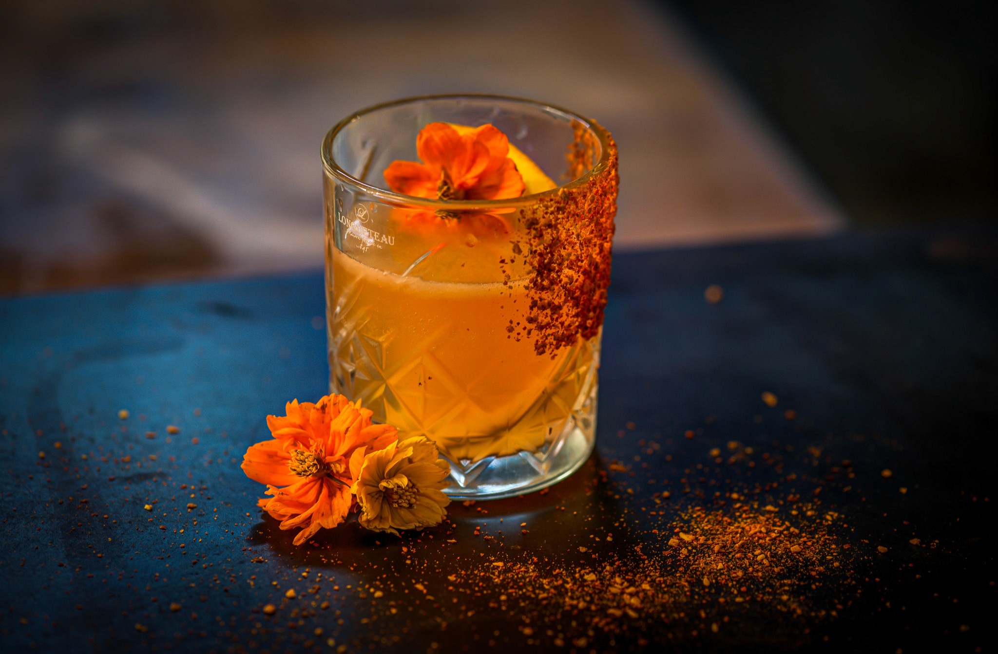 Un cocktail orange sur un bar avec quelques fleurs sur le côté