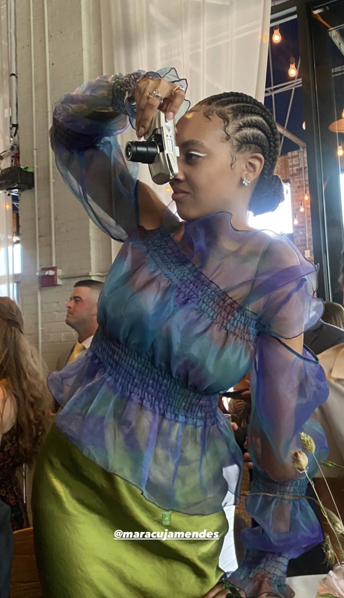 Jess in a colorful organza top holding a point-and-shoot camera to her eye, mid-photo at an event