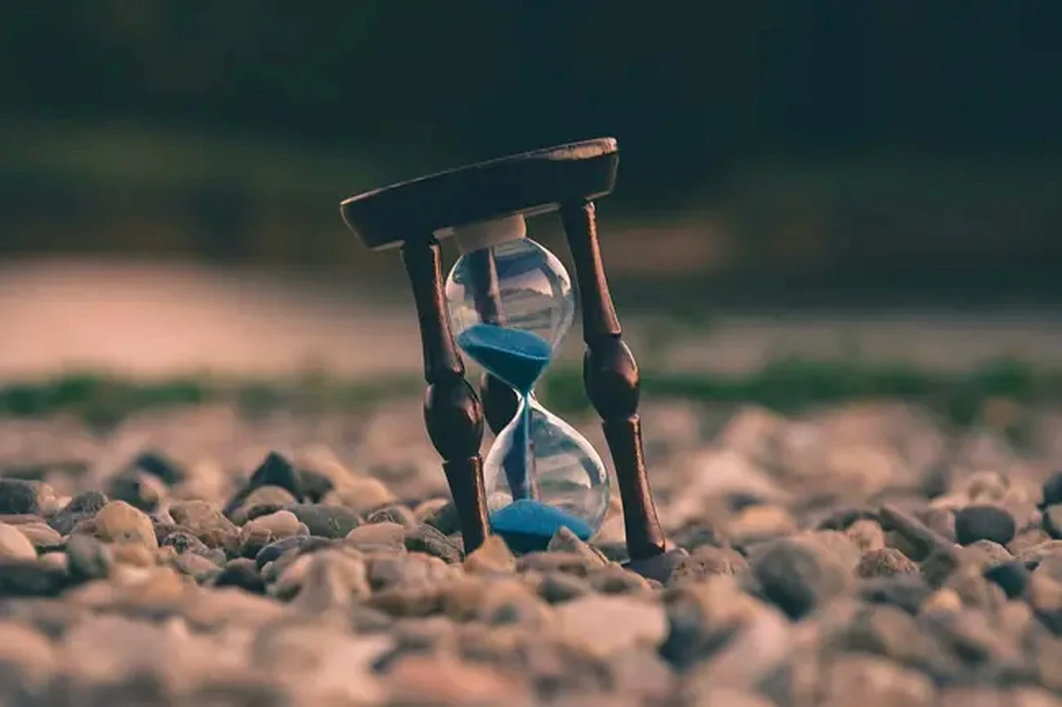 An hourglass with blue sand resting on pebbles
