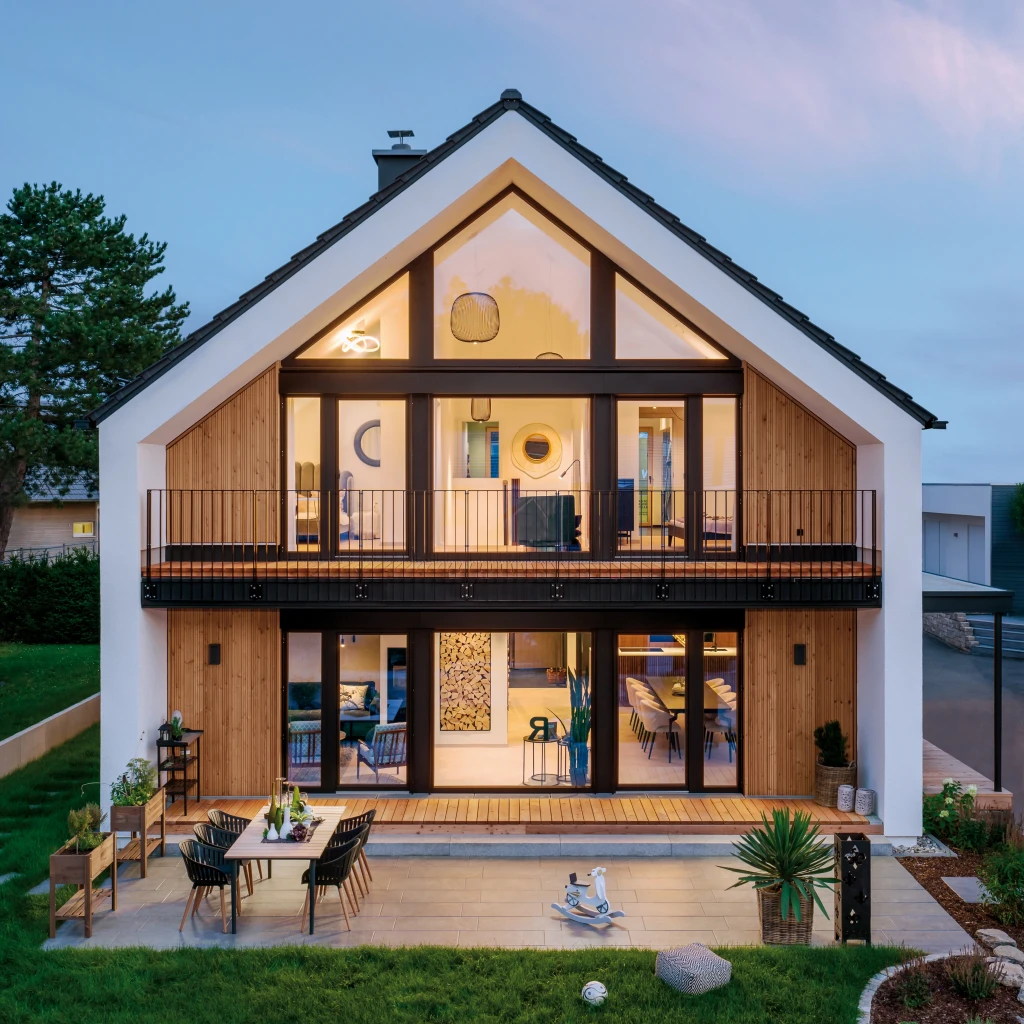 Modernes Einfamilienhaus mit großen Fensterfronten, Balkon und Terrasse mit Sitzbereich und Gartenmöbeln.