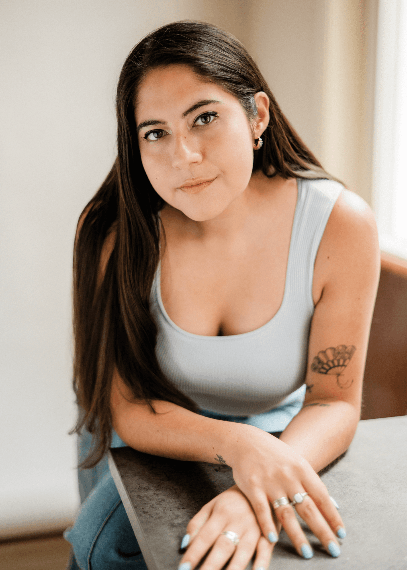 headshot casting photo of Viviana Cardenas, actor, dark-haired woman in grey top, leaning on a table.