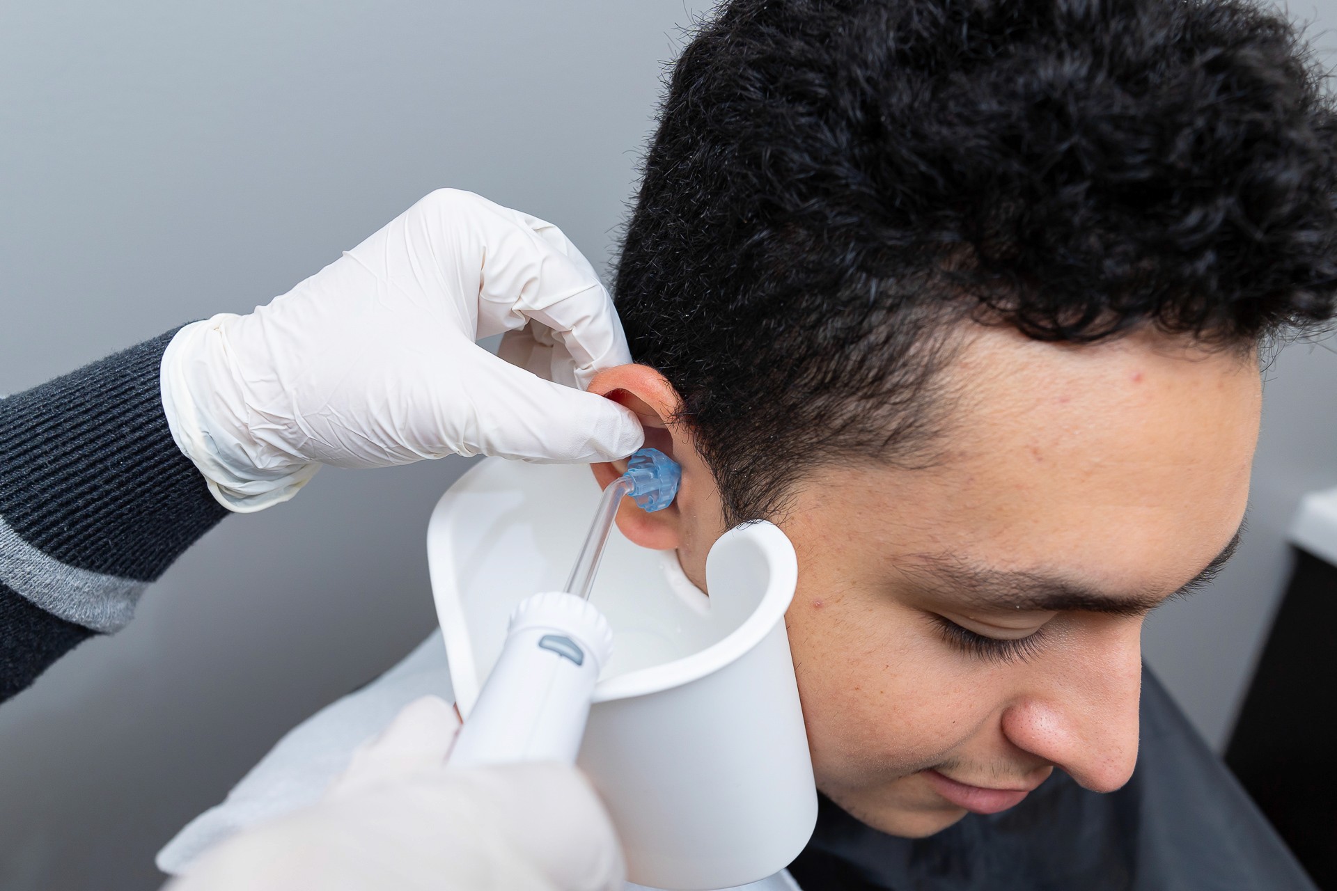 A healthcare professional wearing gloves and a mask examines a patient's ear with a medical instrument.