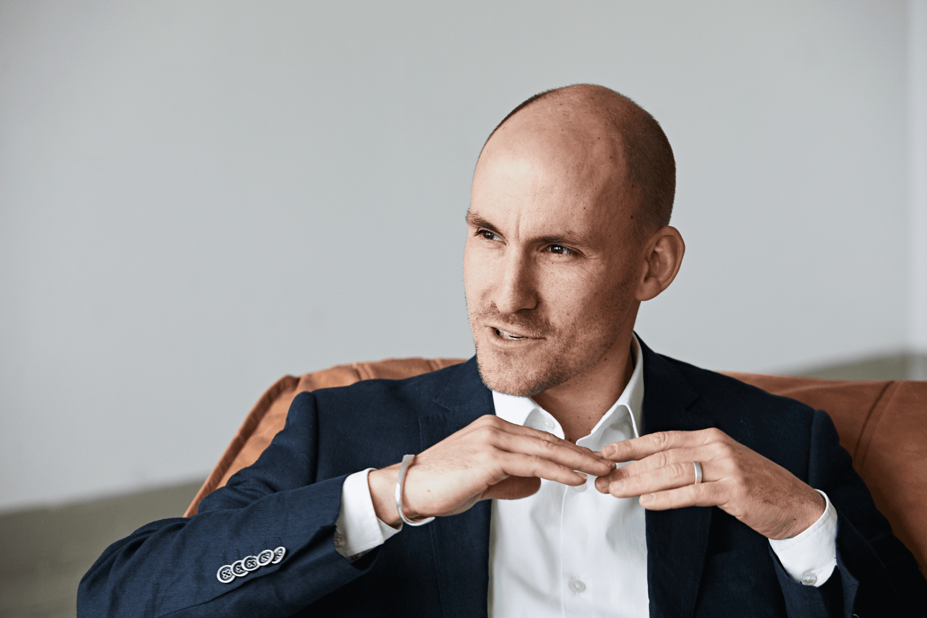 Bald man in suit adjusting his shirt collar.