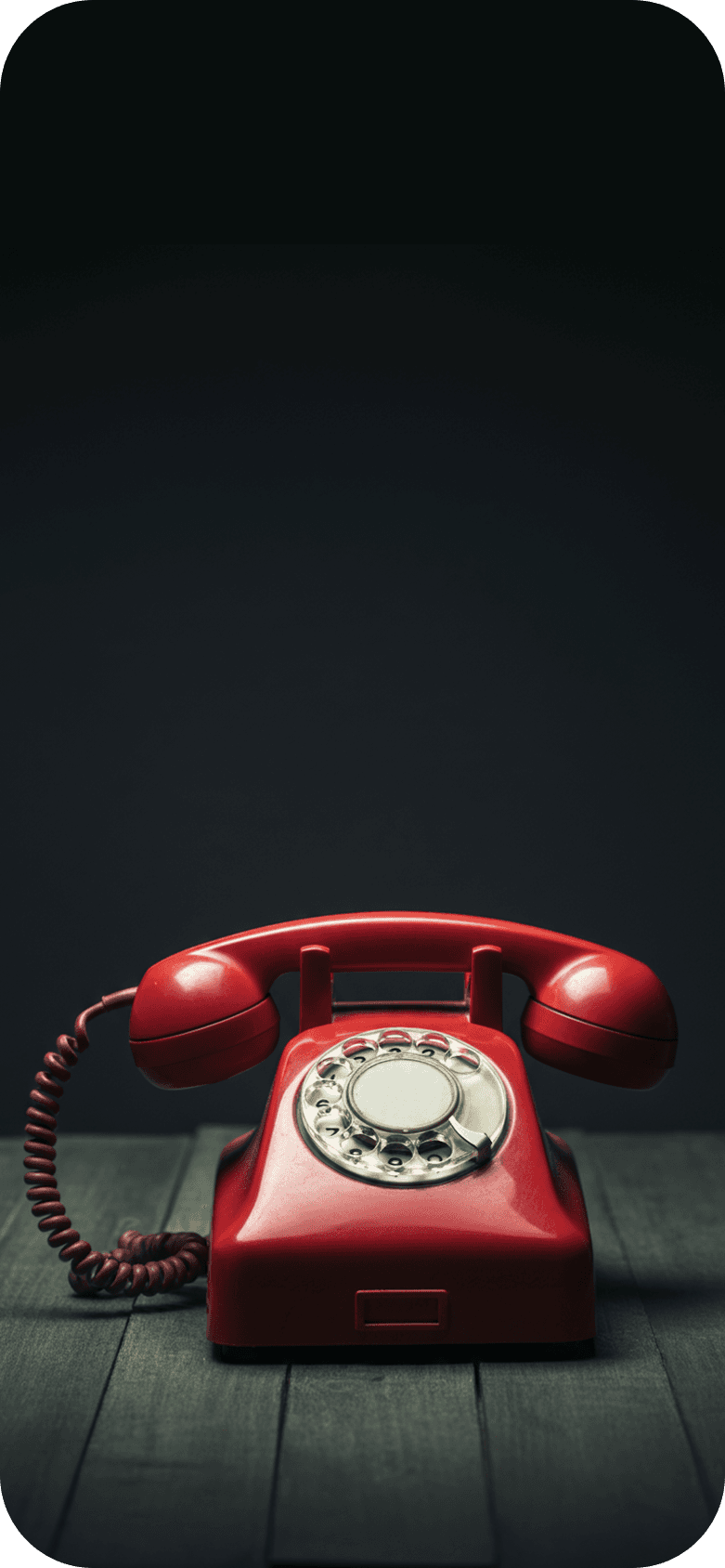 A red, ringing rotary phone sitting on a wood table