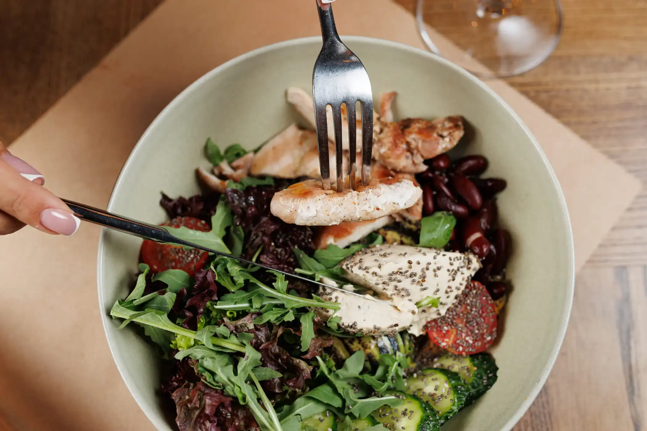 Close-up of a fork lifting grilled chicken from a fresh salad bowl