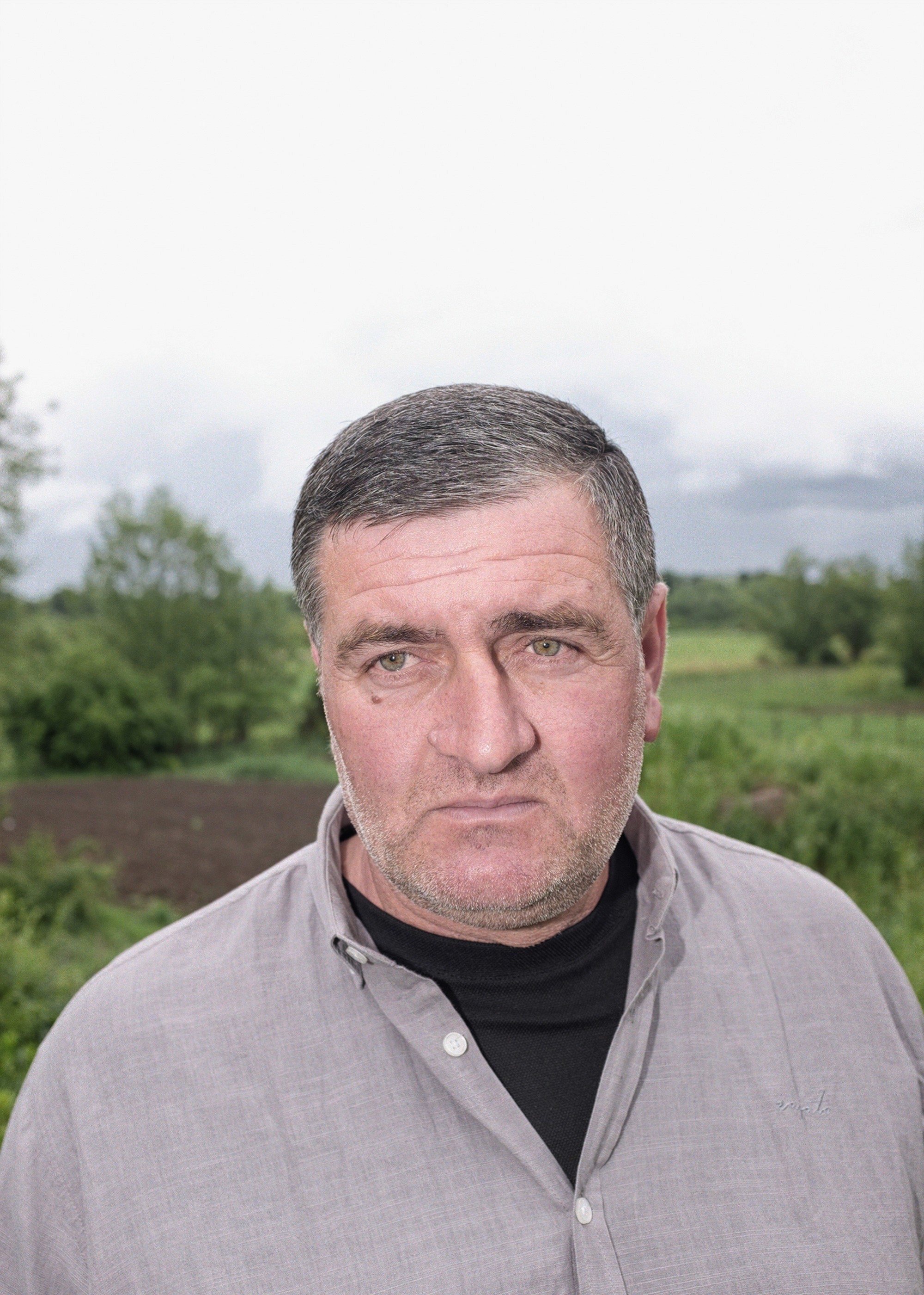 Portrait of a middle-aged Georgian man standing in a green rural landscape, looking directly at the camera.