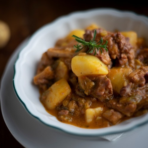 Isang mangkok ng nilagang karne at patatas na nilagyan ng isang sanga ng rosemary.
