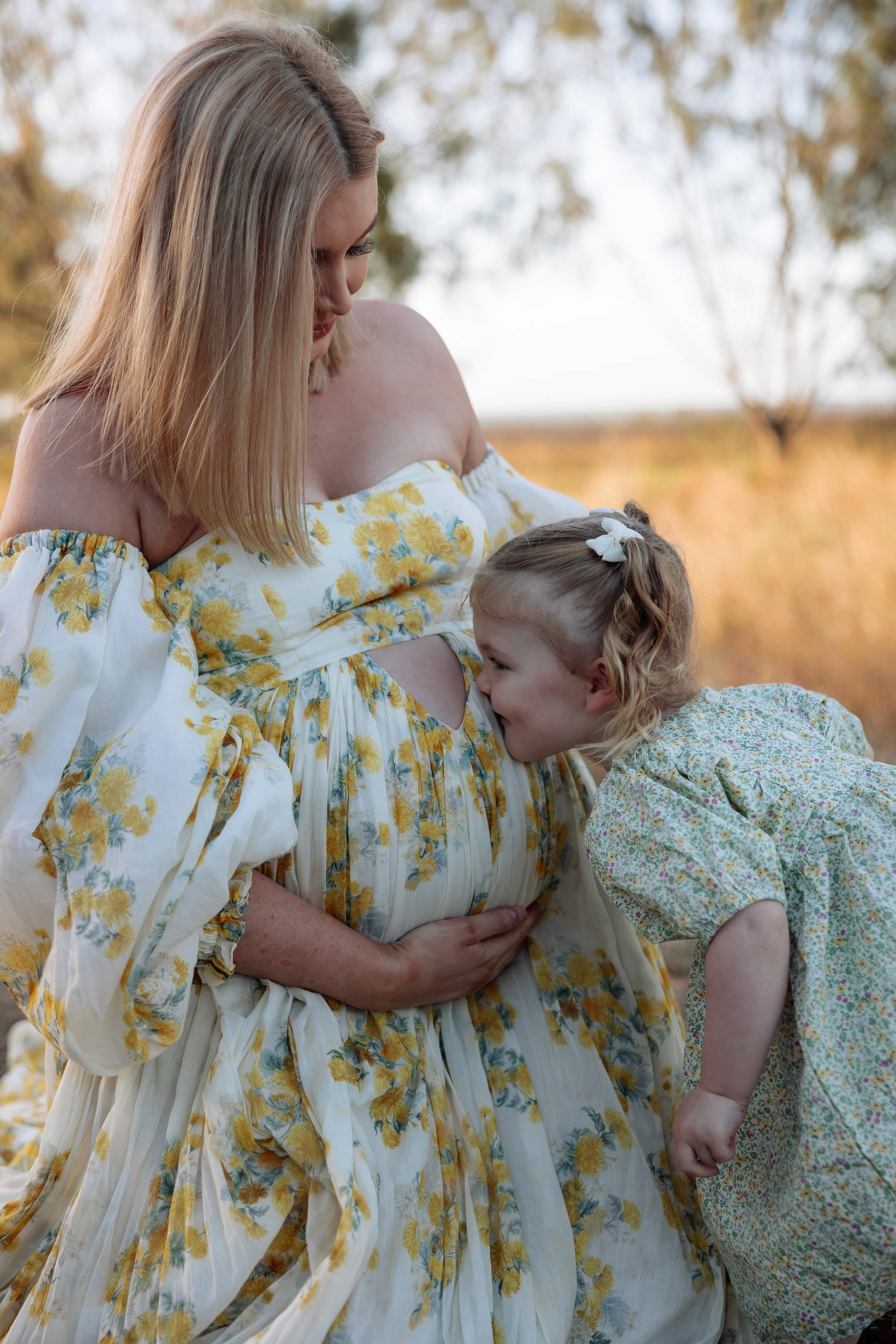 Sibling kissing mothers baby belly in outdoor maternity photoshoot mackay