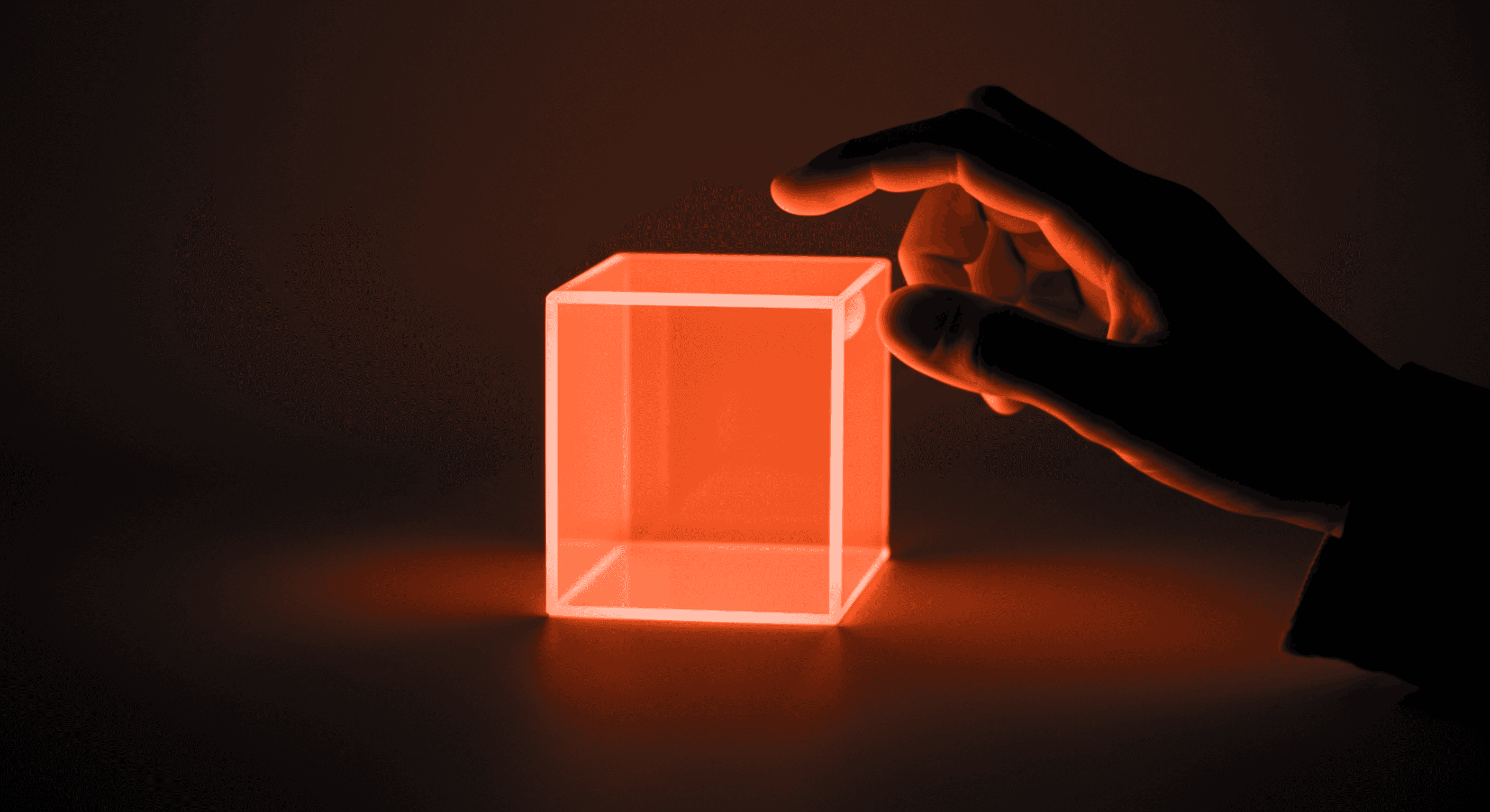 A hand reaches toward a glowing orange cube, casting light in a dark setting.