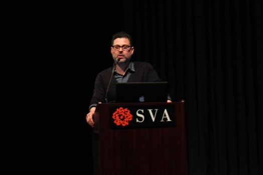 A photo of a man giving a lecture at a stand with SVA logo on it.