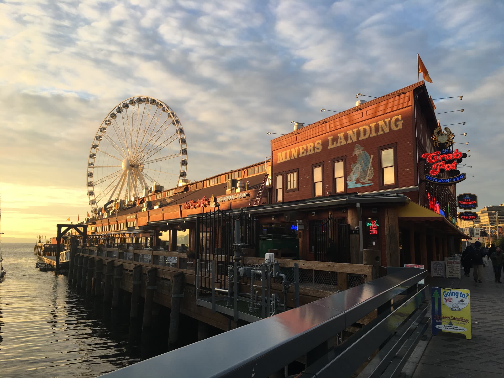 The Seattle Great Wheel and the Miners Landing pier buildings lit by low sunset light, with Elliott Bay at left.
