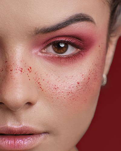 Fotografia portretowa przedstawiająca zbliżenie na twarz modelki z mocnym makijażem artystycznym, którego kolorem przewodnim jest czerwony