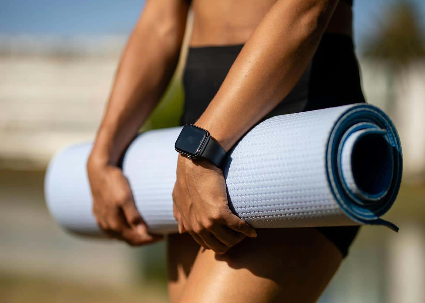 Person wearing an Apple Watch outdoors holding a rolled yoga mat in front of them