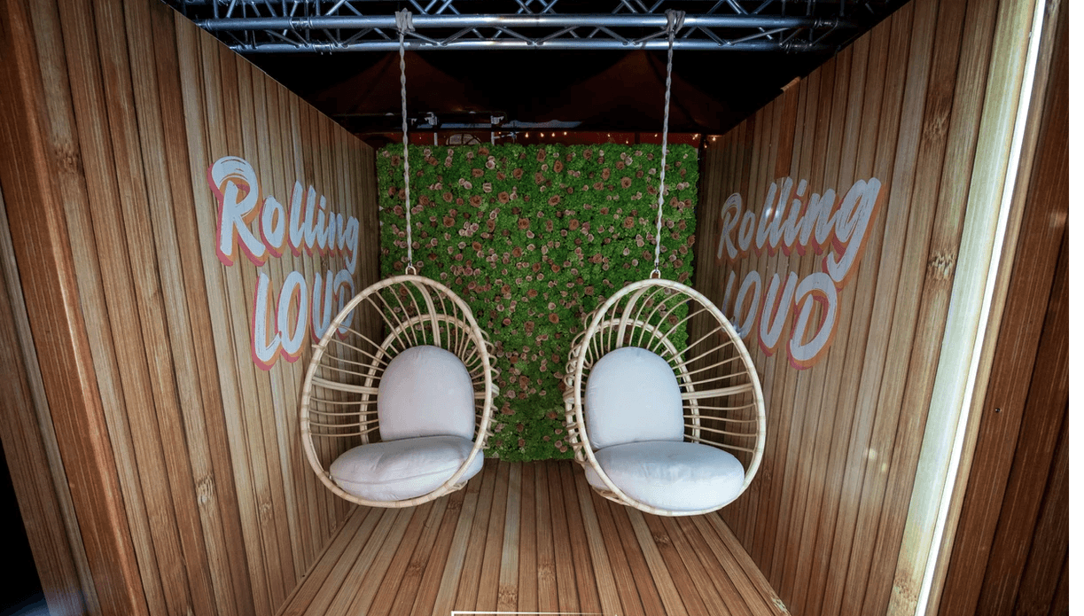 Rollin’ Loud lounge style photo moment with two hanging chairs inside a wood booth with greenery wall.