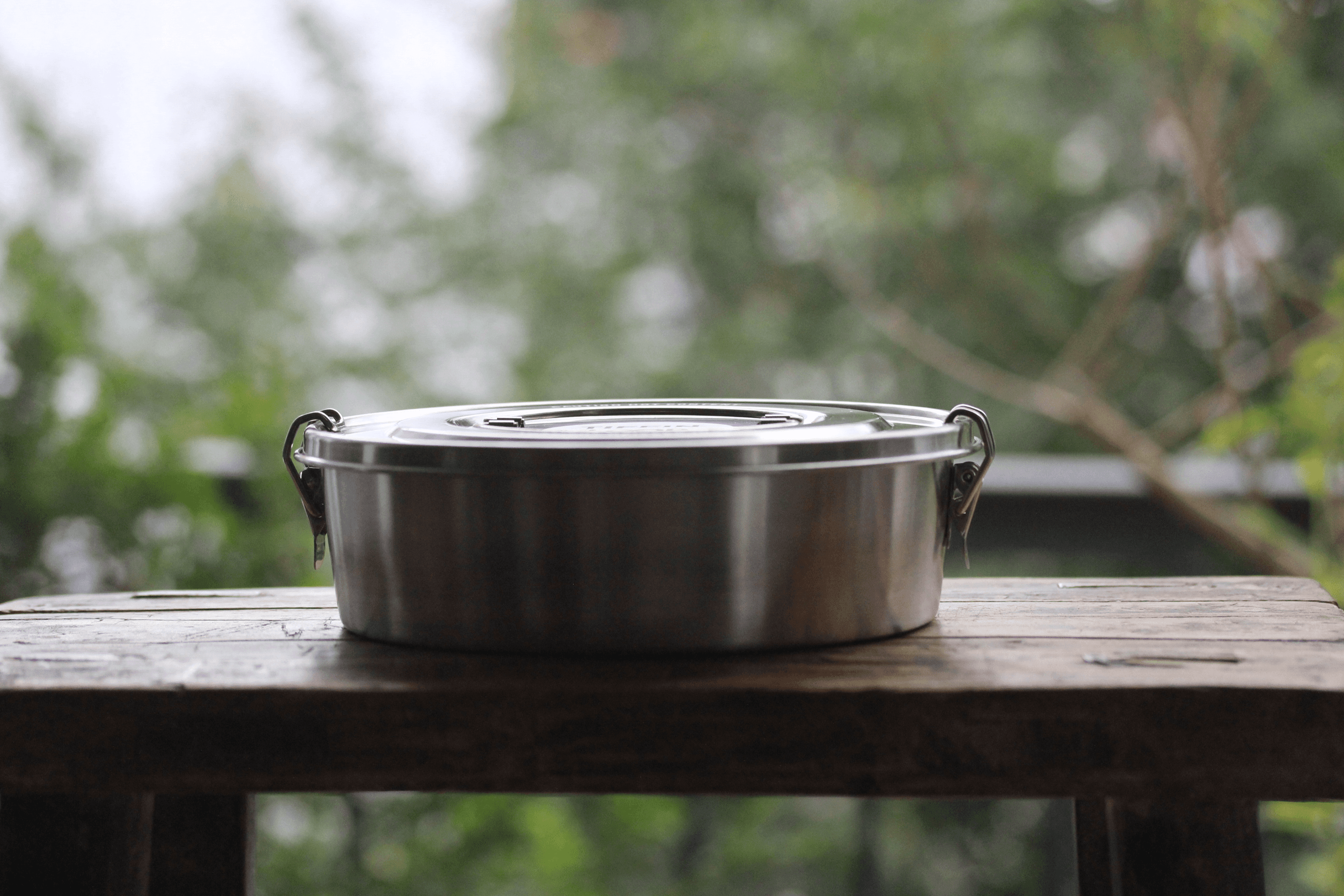 Round metal container with latches on a wooden table.