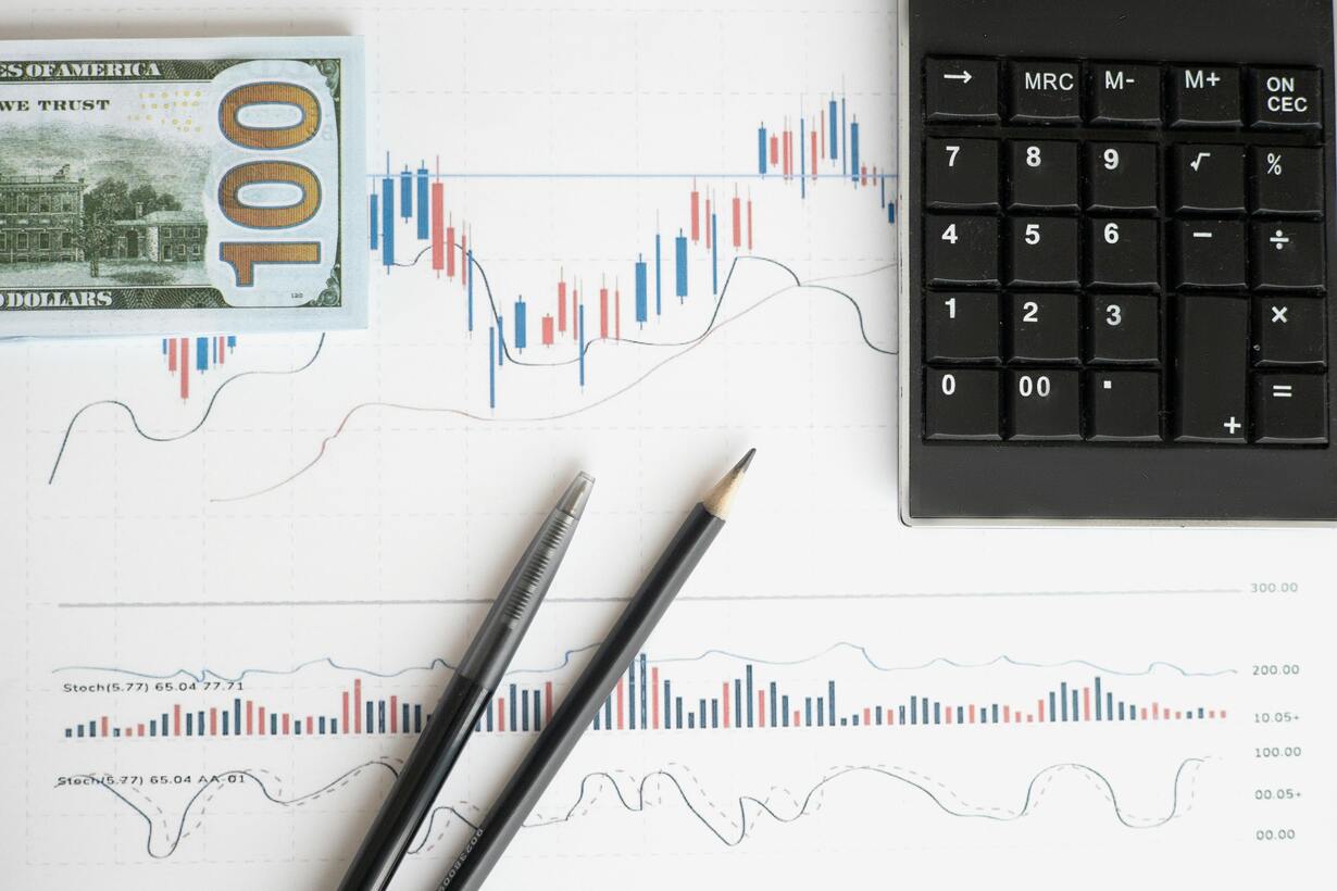 Finance concept: U.S. $100 bill, stock market chart, calculator, pen and pencil on a table