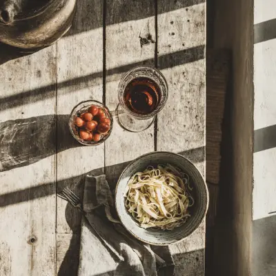 an overhead shot of a casual Italian lunch setting with pasta and a glass of red wine, rustic ceramic plates, linen napkin, soft shadows from window light, wooden table, warm and inviting mood, minimal styling, elegant but approachable, film photography look