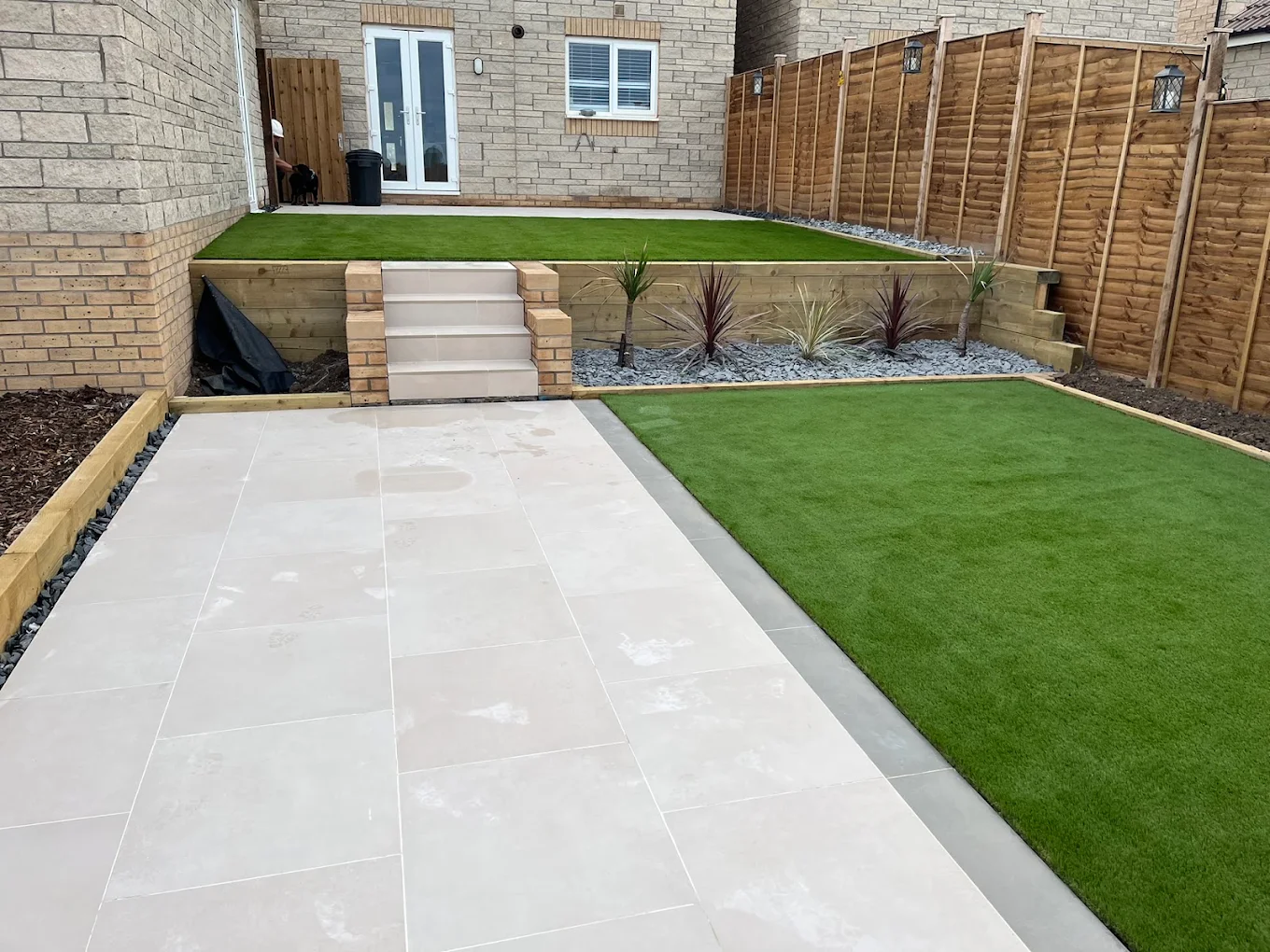 Completed garden with pale paving, artificial lawn, raised terrace and steps, and timber fencing by Bartec Landscape & Build.