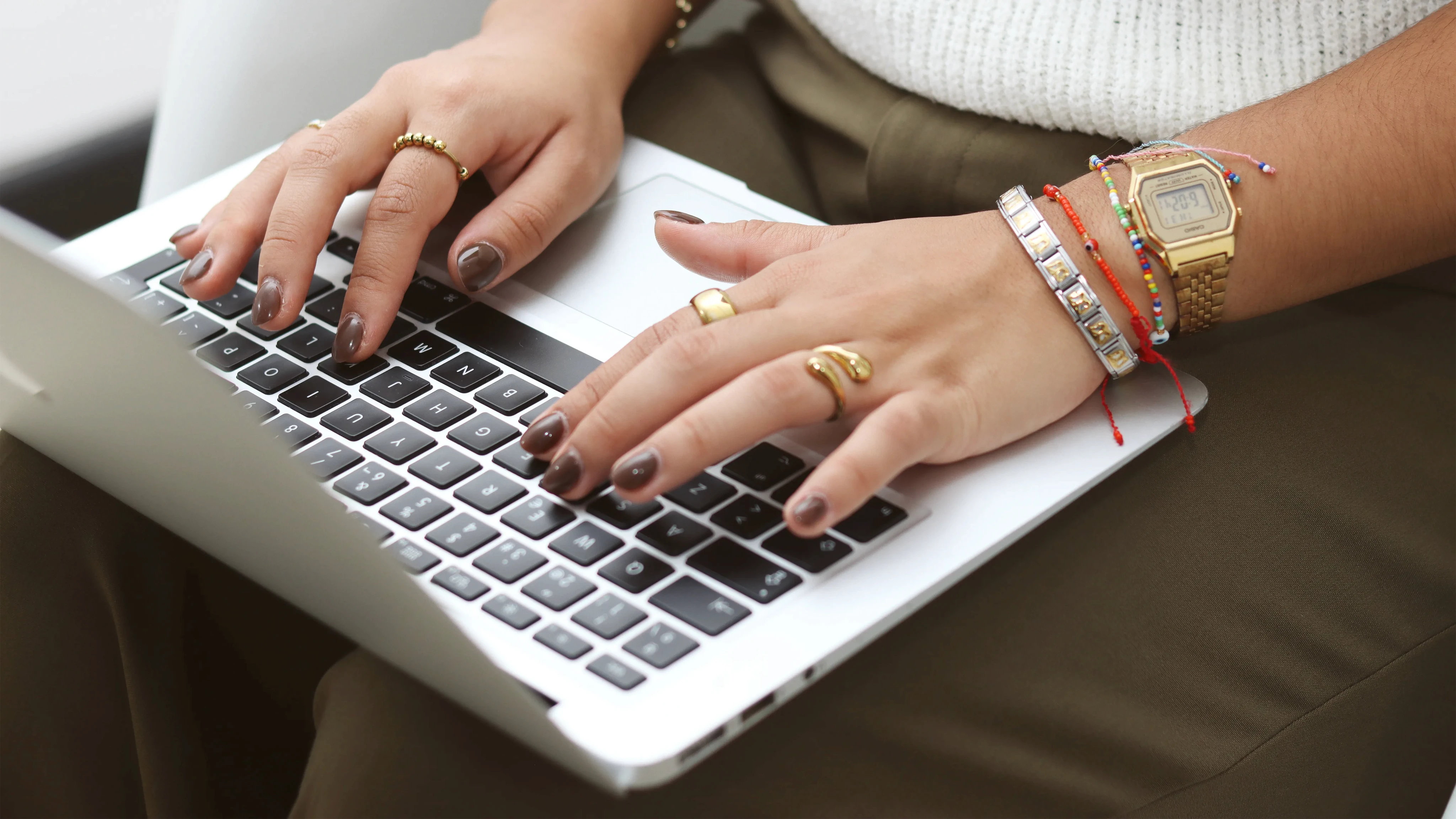 Manos femeninas escribiendo en laptop plateada.