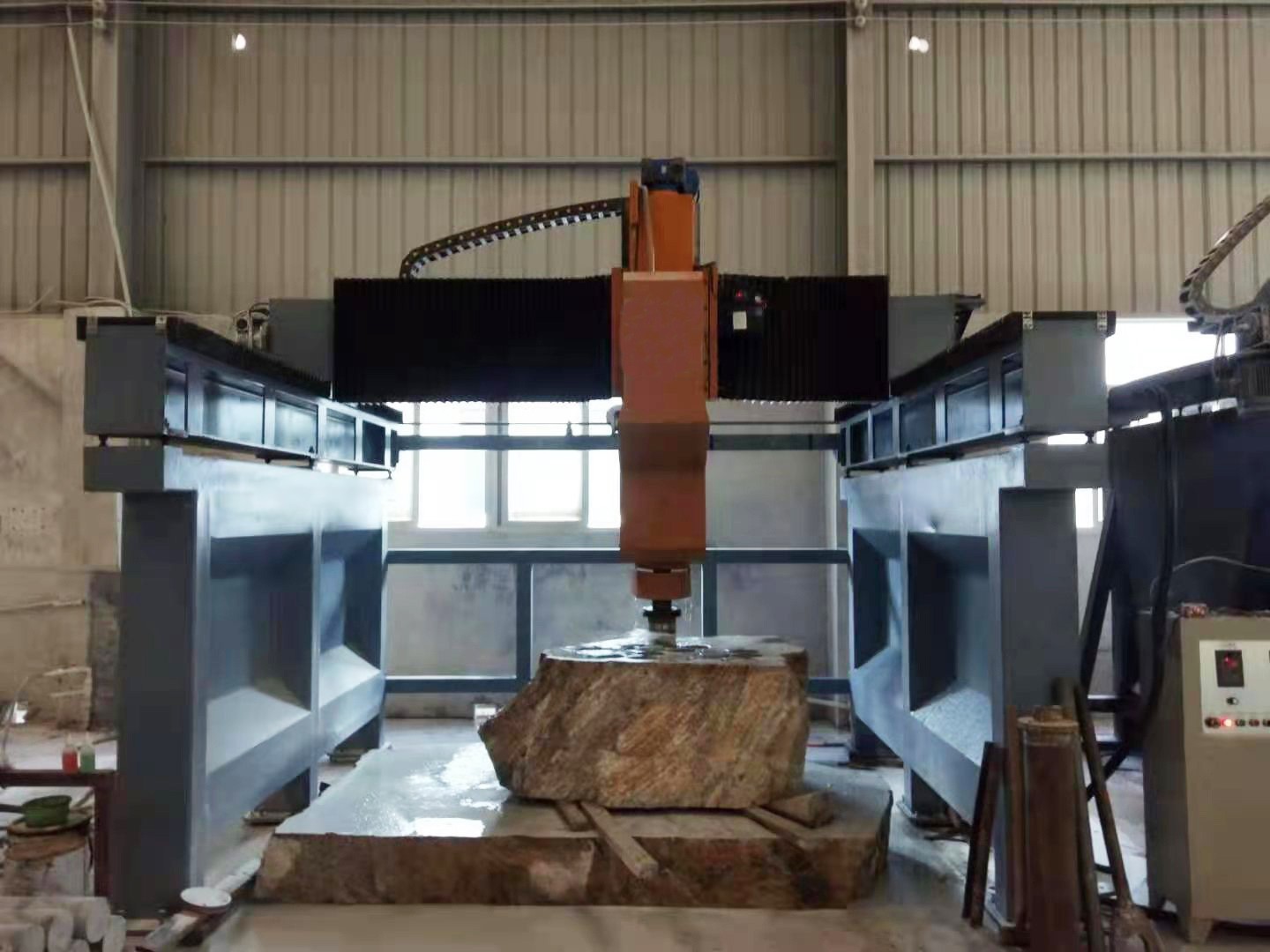 Gantry type CNC drilling machine in operation, processing a large stone block in an industrial setting, demonstrating its precision and efficiency in handling complex drilling tasks.