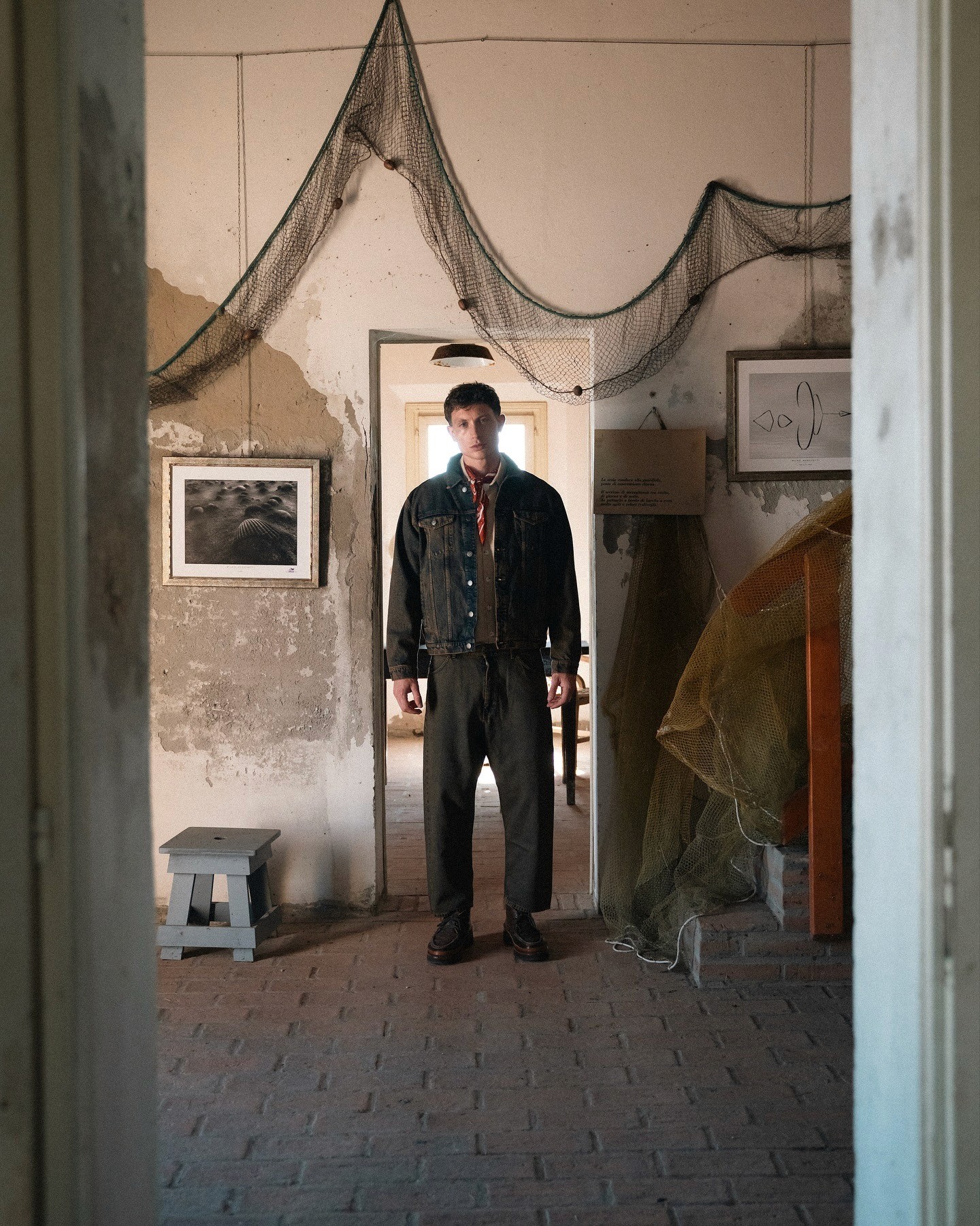 Mannequin portant un look décontracté dans le lookbook FW25 de Wooden Store, à l'intérieur d'une maison de pecheur