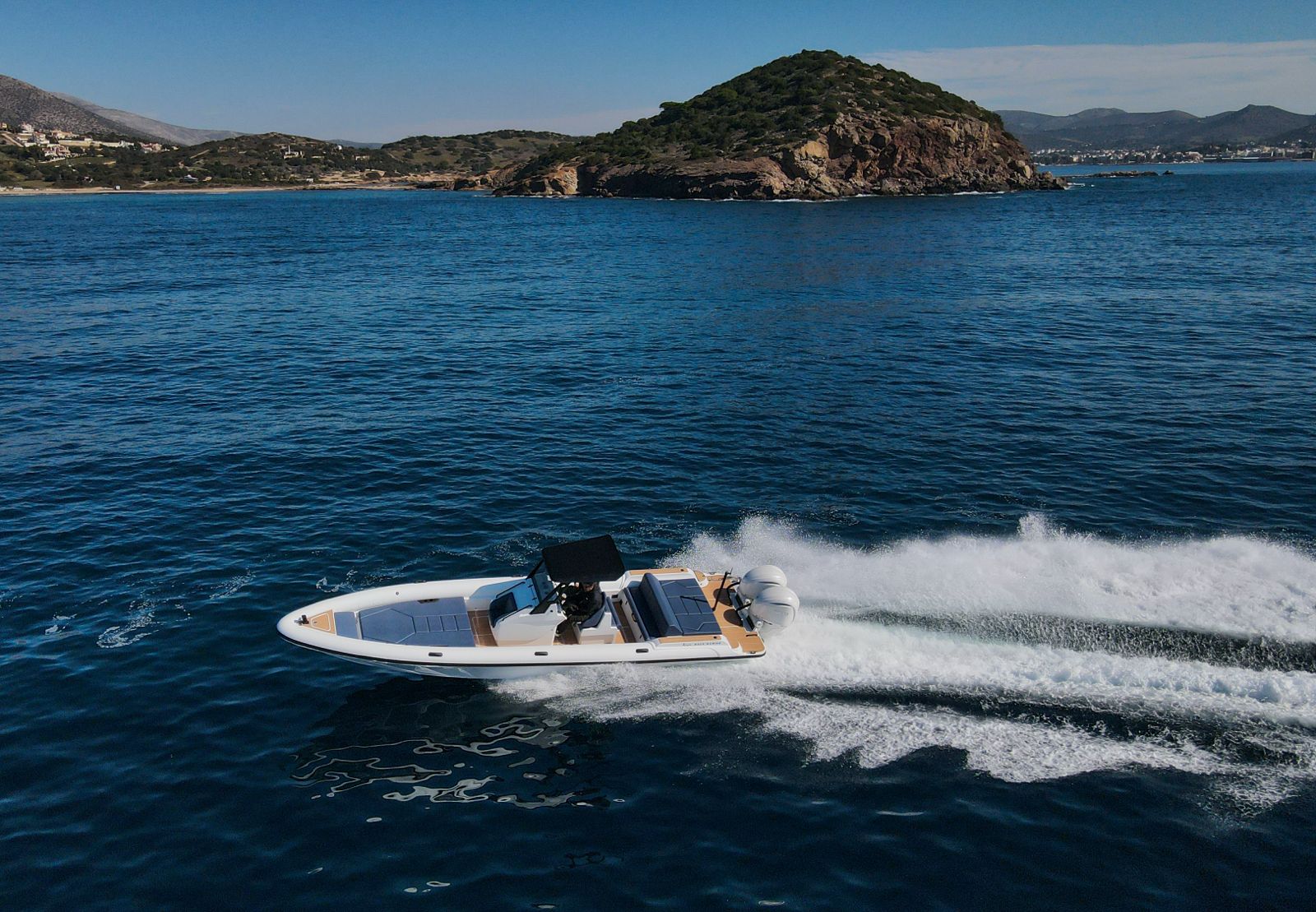 White Rock 36 speedboat with captain at helm cruising calm blue waters near Paros coastline with hills in background.