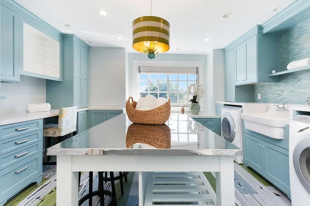 'Port Streets Remodel' laundry room with light blue cabinets, modern appliances, and a striped rug under a green pendant light.