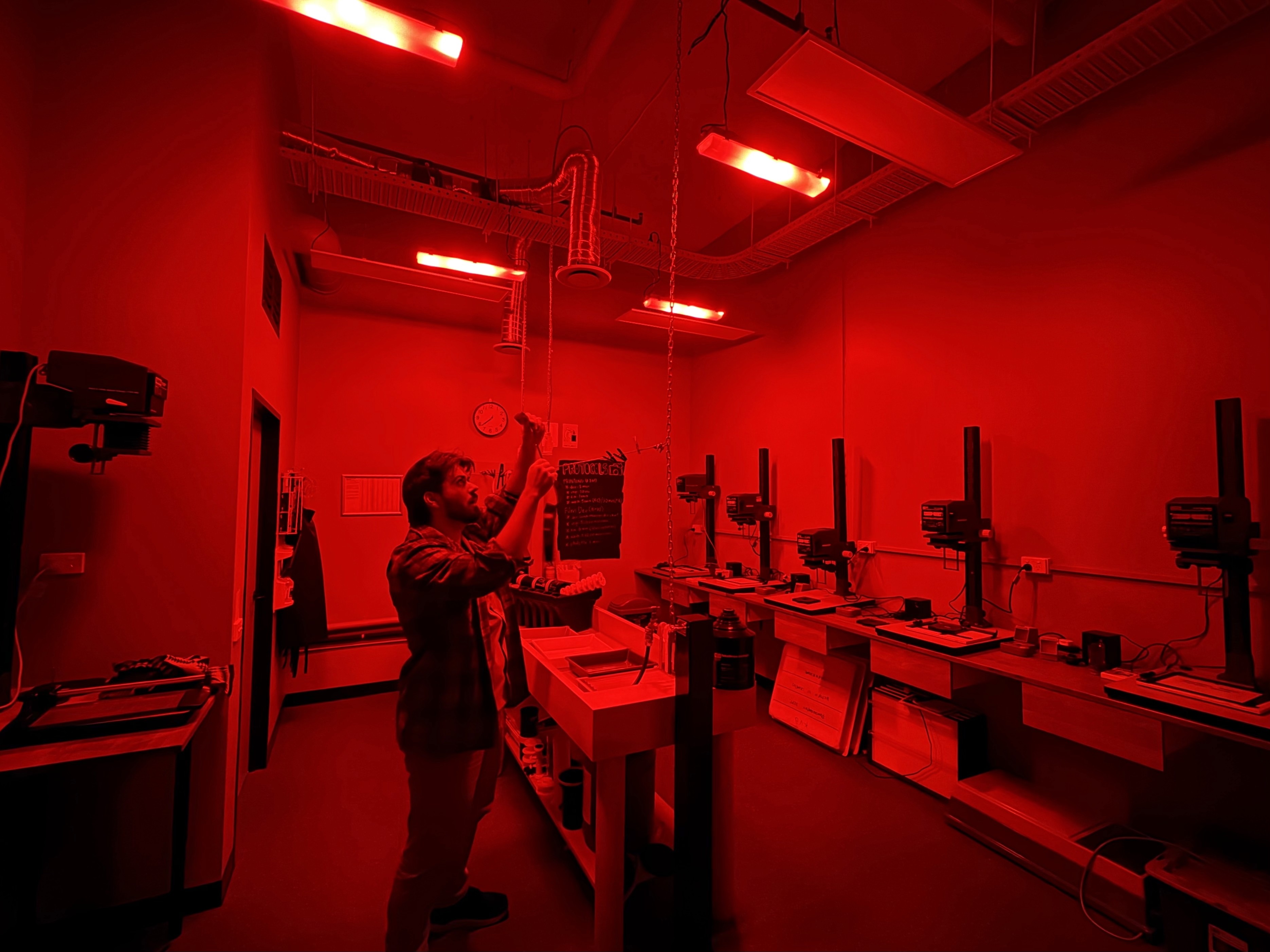 Wide angle view of darkroom with safelight with man inspecting 35mm film