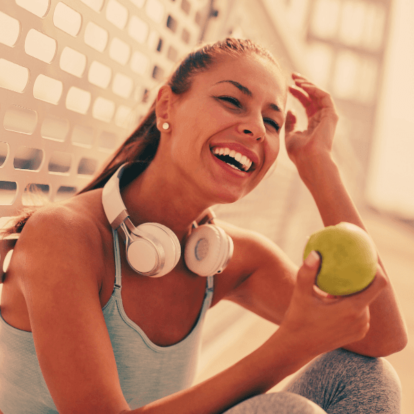 Woman sitting holding a green apple in gray workout wear smilling